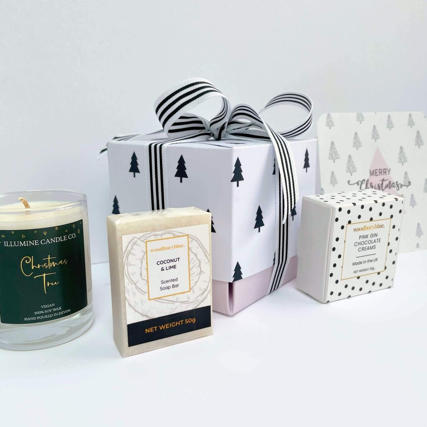 Close-up view of Warm Wishes Gift Box with black tree wrapping, pink tree card, and luxury UK-made contents – candle, soap, and chocolate.