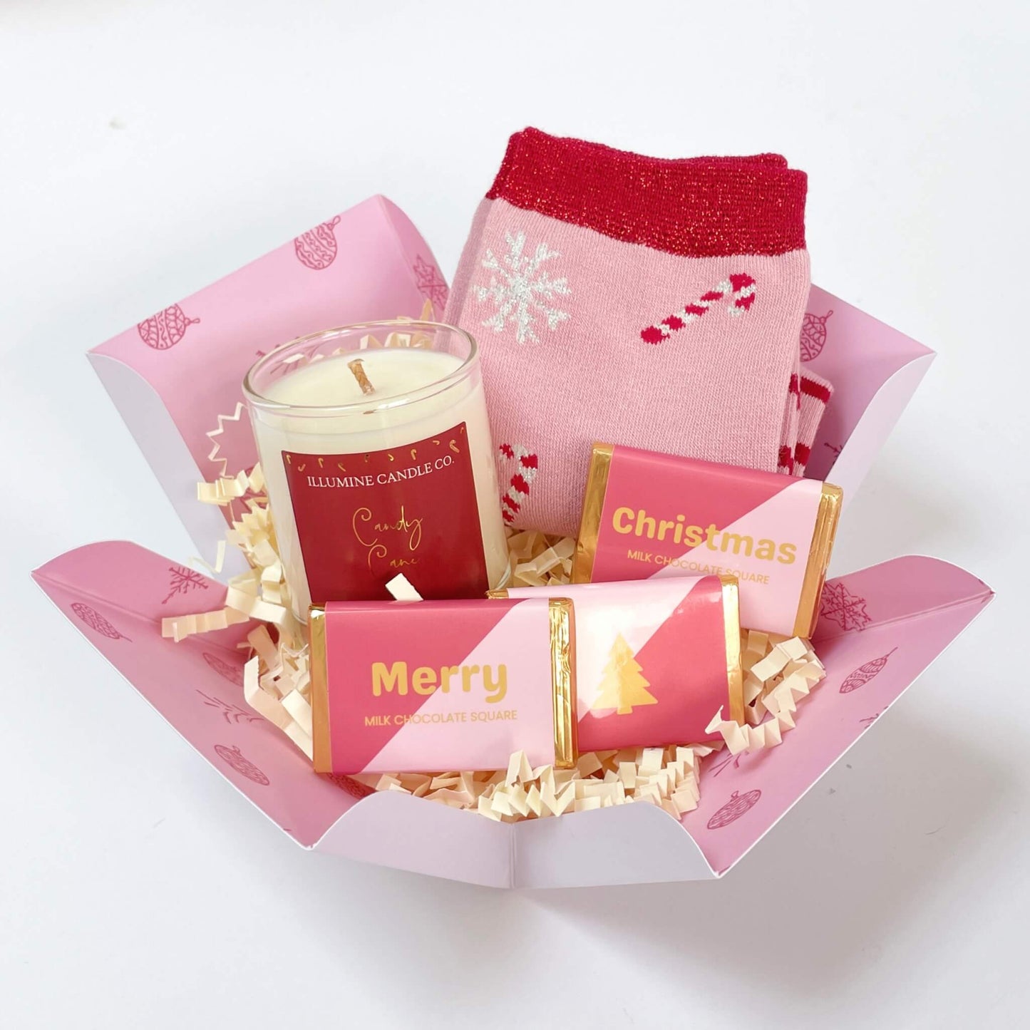 Unboxed Candy Cane Wishes Gift Box featuring a pair of pink festive socks, candy cane scented candle, and three pink and gold Merry Christmas chocolate squares inside a patterned pink open box.