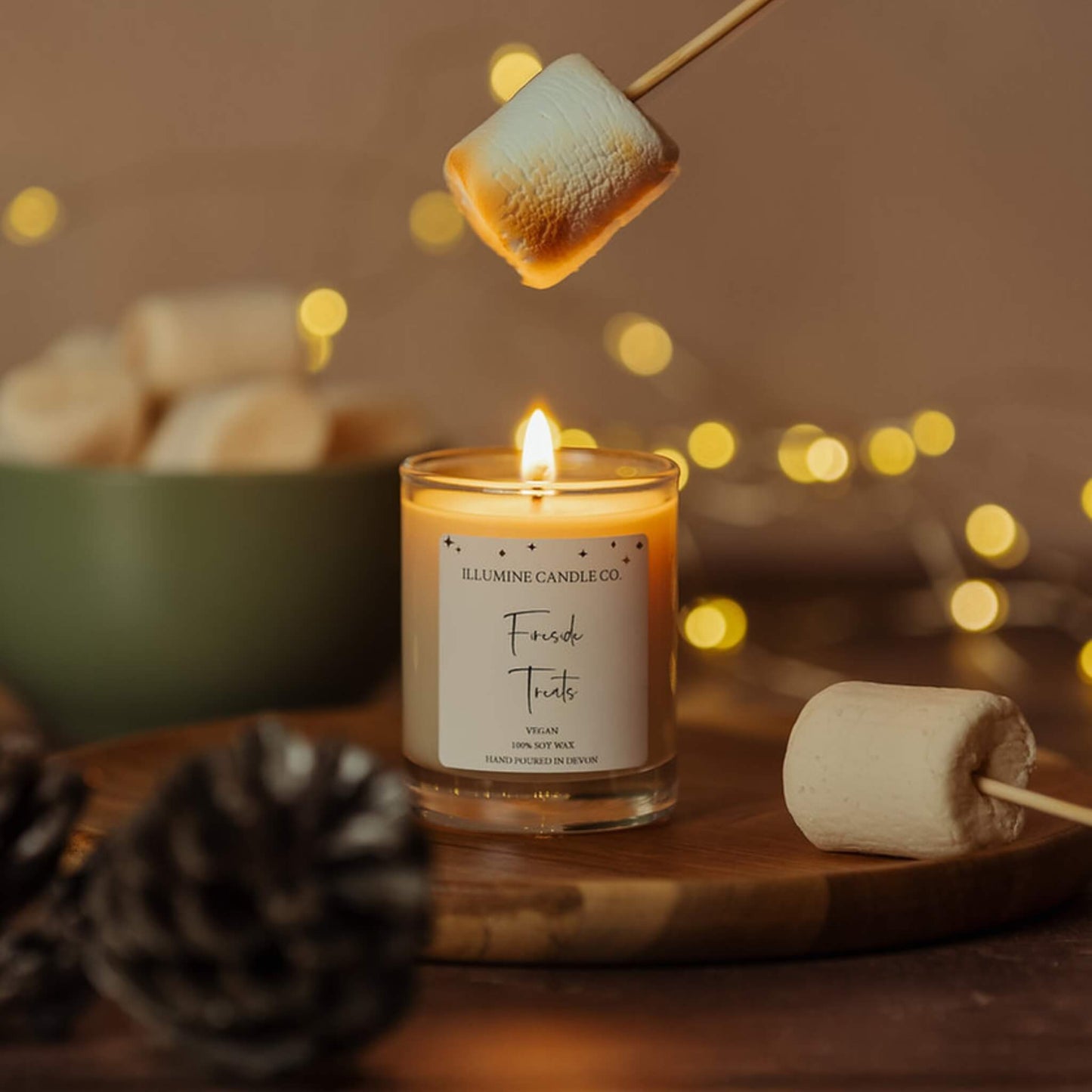 Fireside Treats soy wax candle by Illumine Candle Co with a toasted marshmallow above the flame, warm festive background and fairy lights