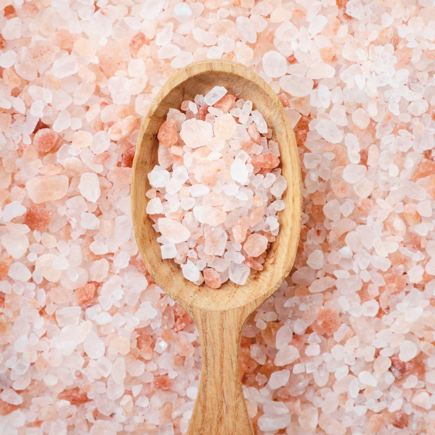 Focus aromatherapy bath salts with coarse Himalayan pink salt crystals in a wooden spoon on pink salt background