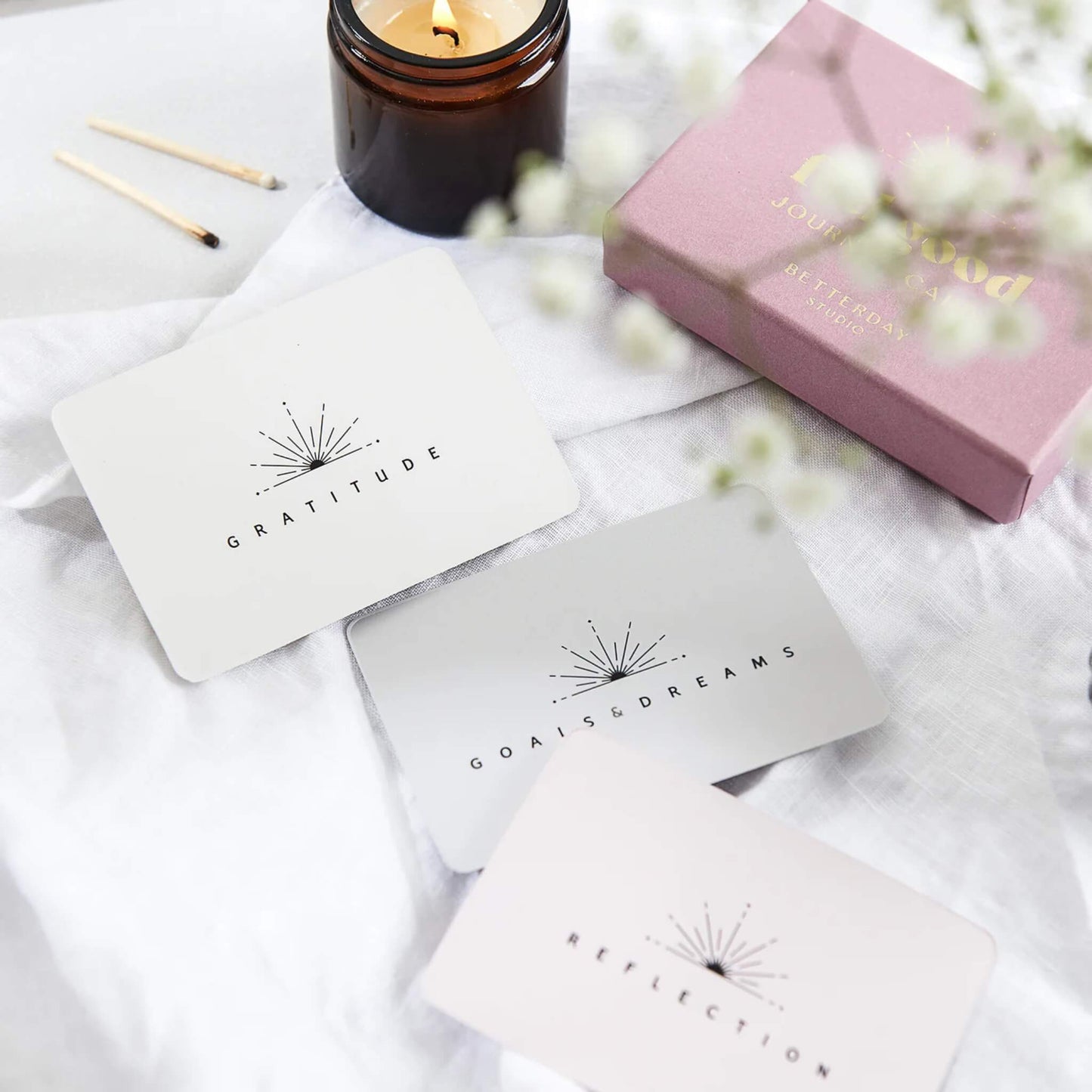 Gratitude, Goals & Dreams, and Reflection cards styled with a candle, matches, and a pink gift box on a soft white fabric backdrop.