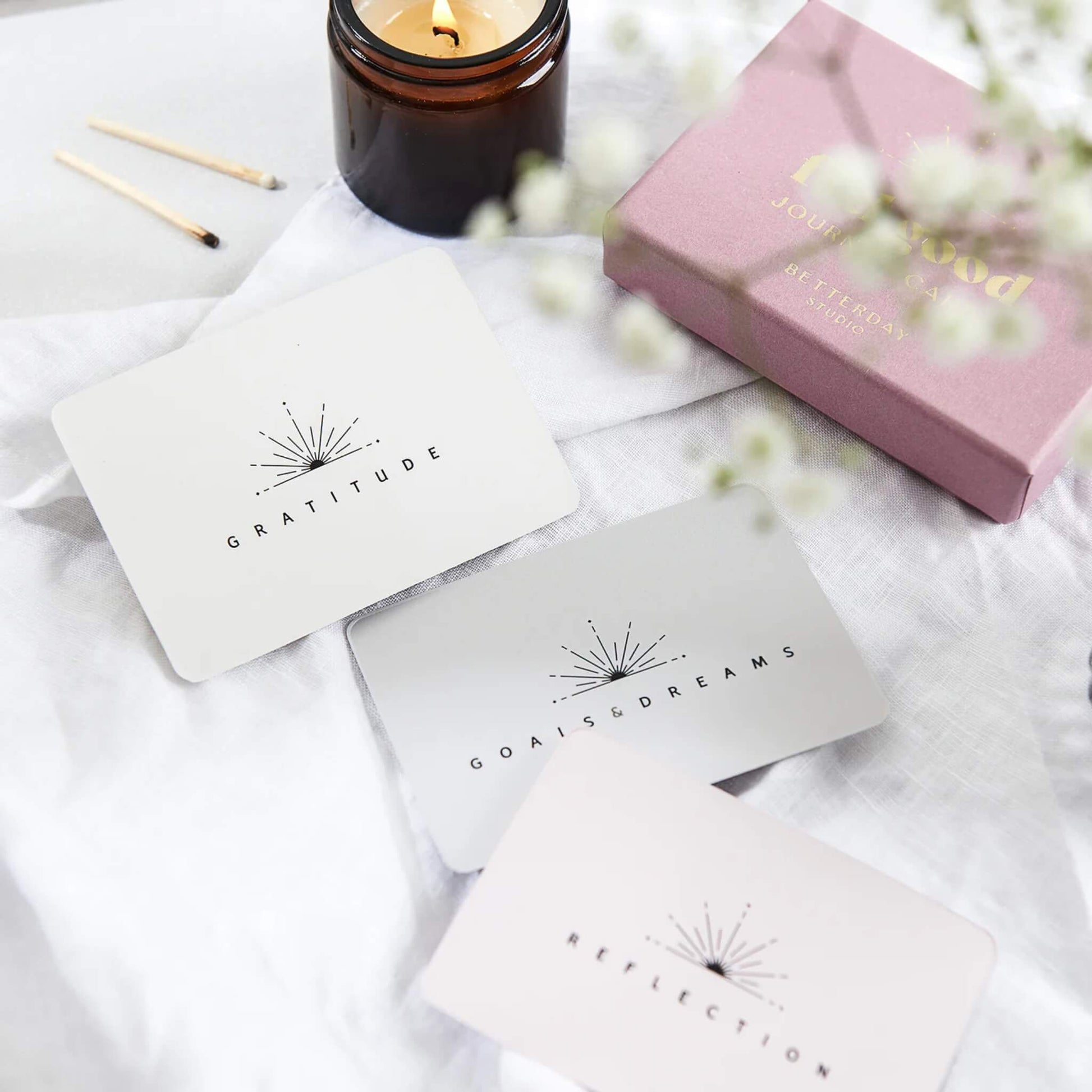 Gratitude, Goals & Dreams, and Reflection cards styled with a candle, matches, and a pink gift box on a soft white fabric backdrop.