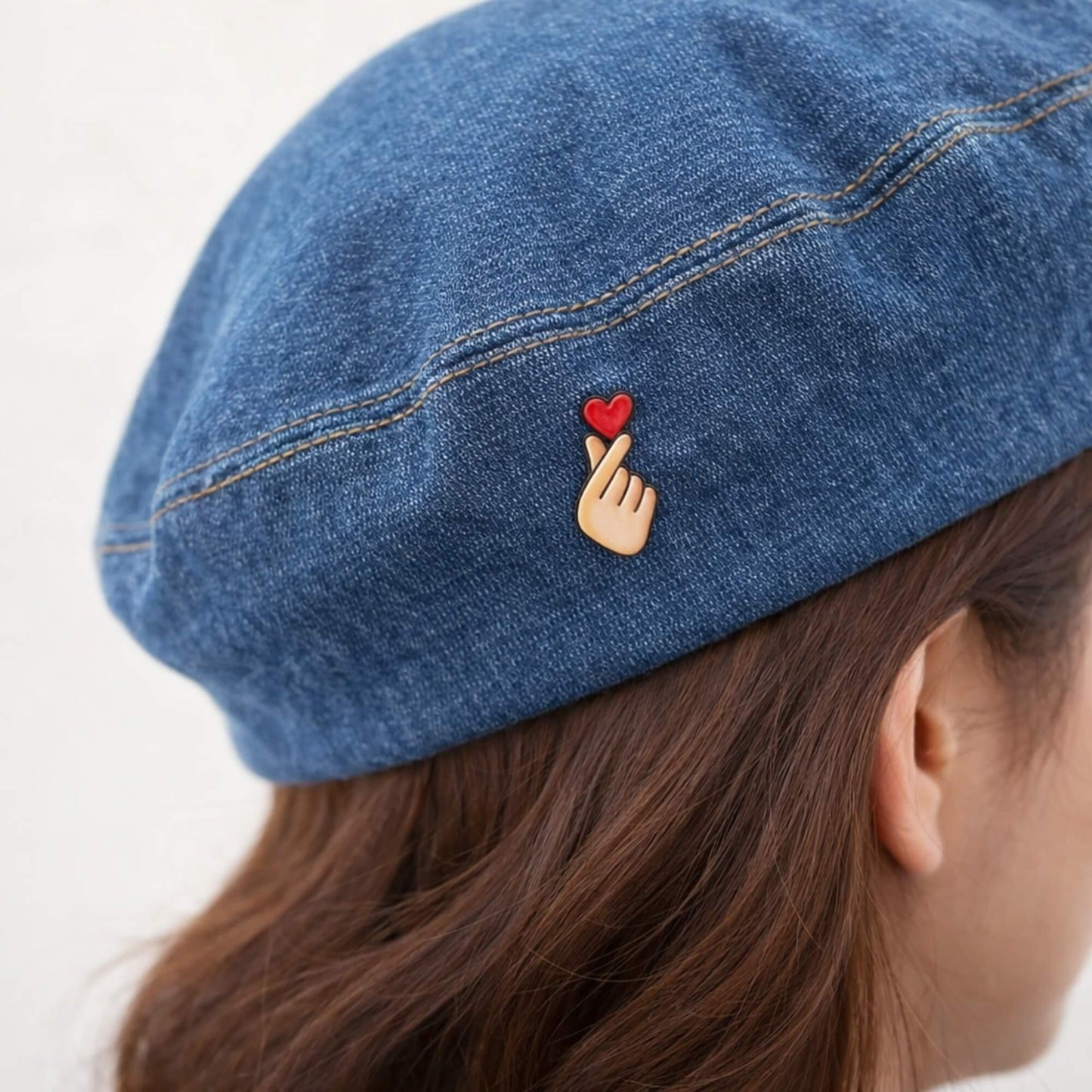Hand holding heart enamel pin badge worn on a denim beret
