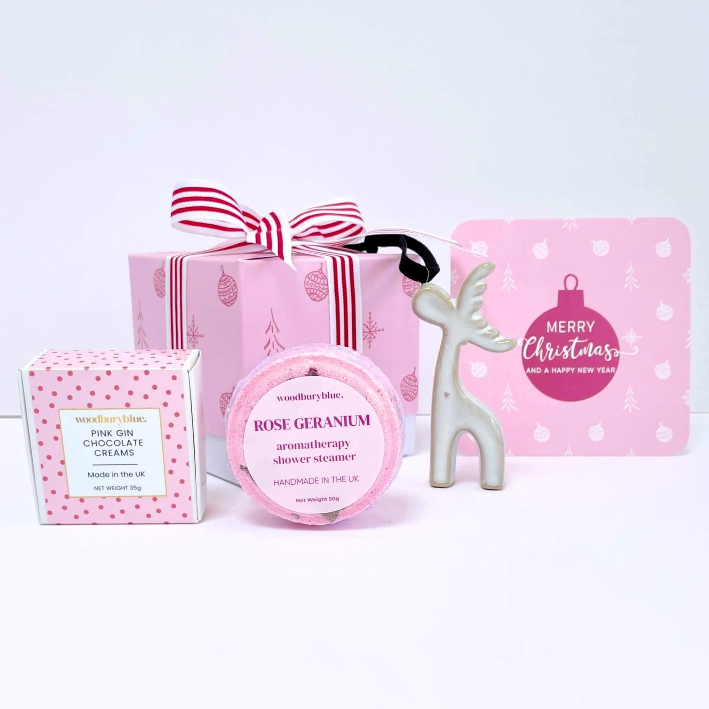 Collection of Christmas-themed products including a box of chocolates, rose geranium shower steamer, a reindeer tree decoration and Christmas card on a white background