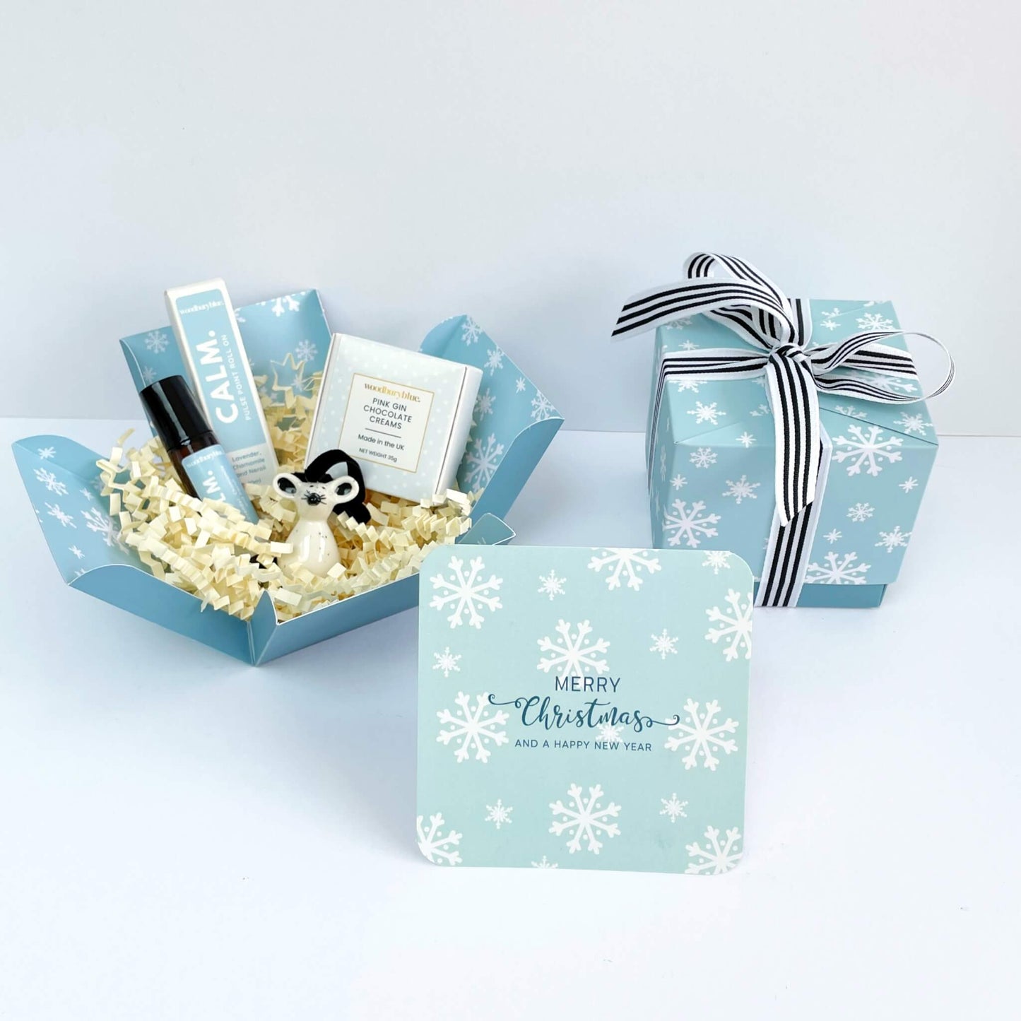 Open Silent Night Christmas gift box filled with Calm roll-on, pink gin chocolates, ceramic mouse and cream shred, shown with blue snowflake notecard.