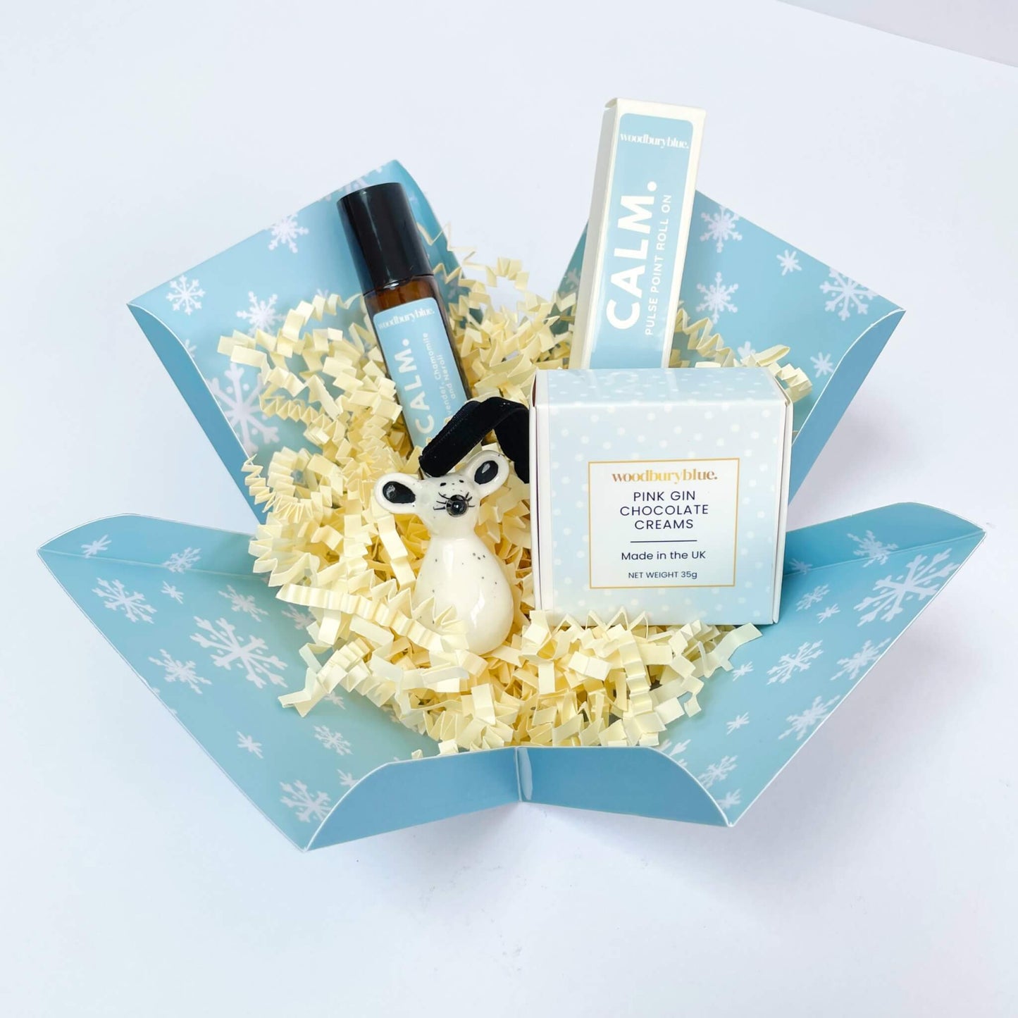 Unboxed Silent Night Christmas Gift Box featuring shredded filler, Calm aromatherapy roll-on, ceramic mouse and chocolates in a snowflake box.