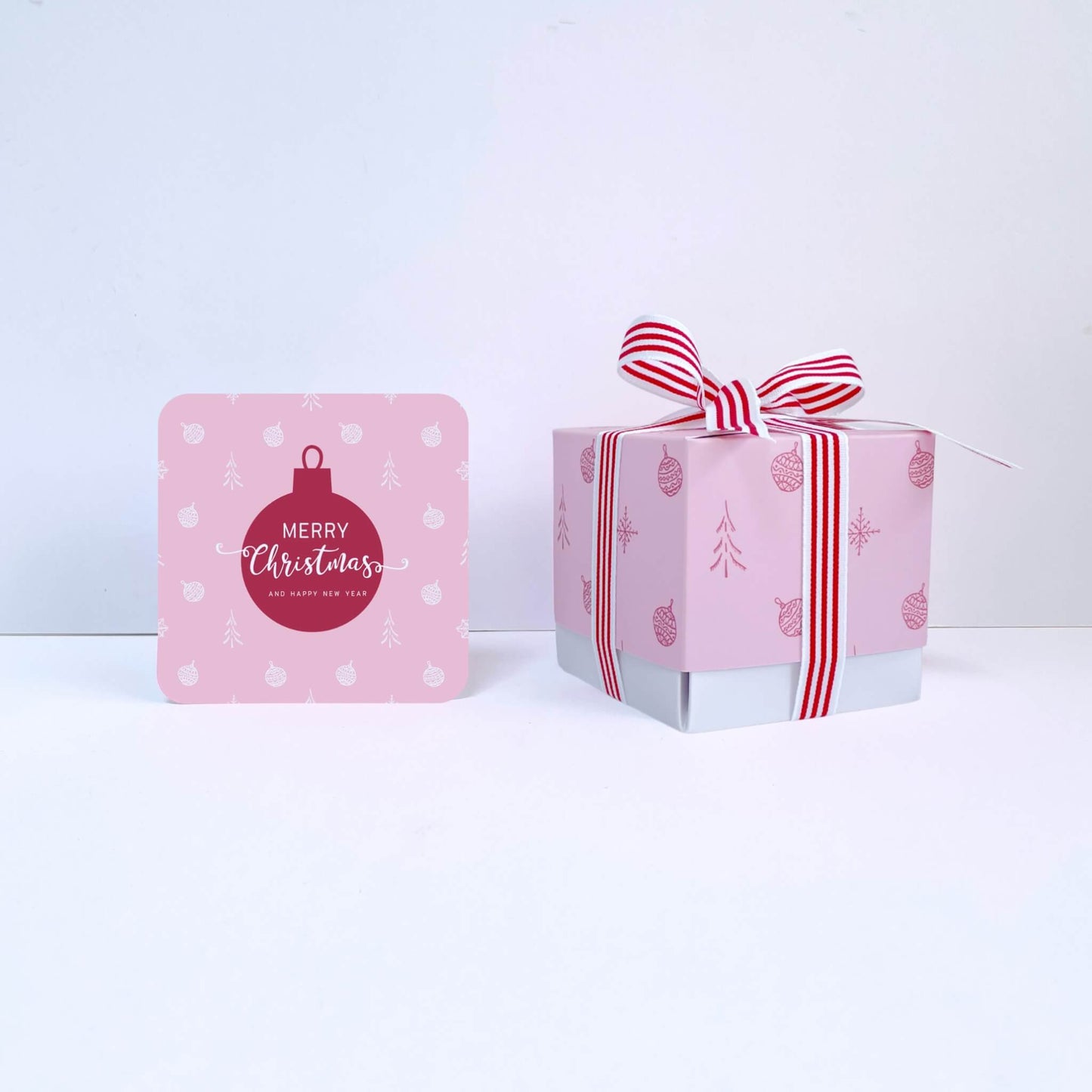 Pink Christmas gift box with a striped
red ribbon and a matching card on a white background