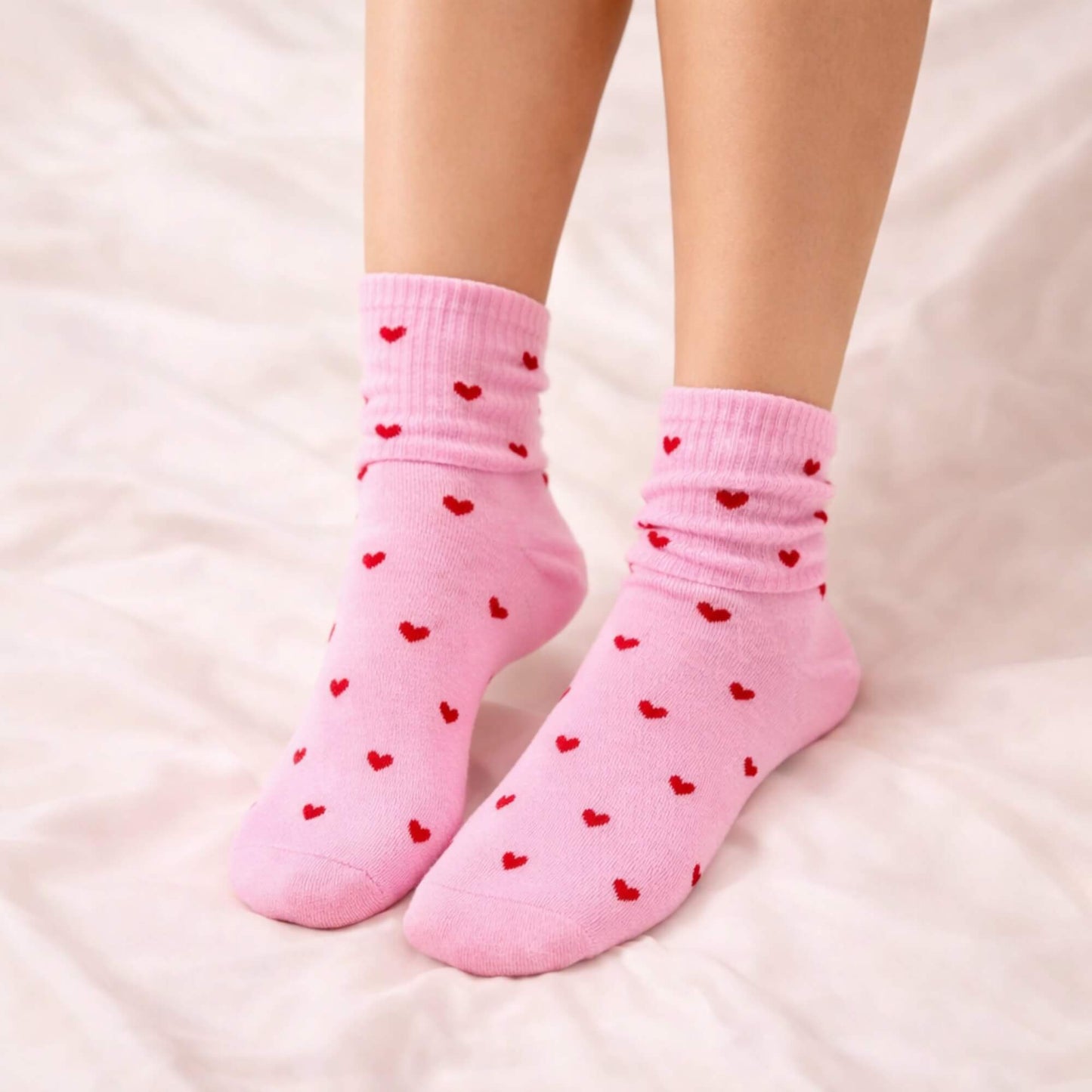 Pink socks with small red hearts being worn, shown from the ankle down on a soft neutral background