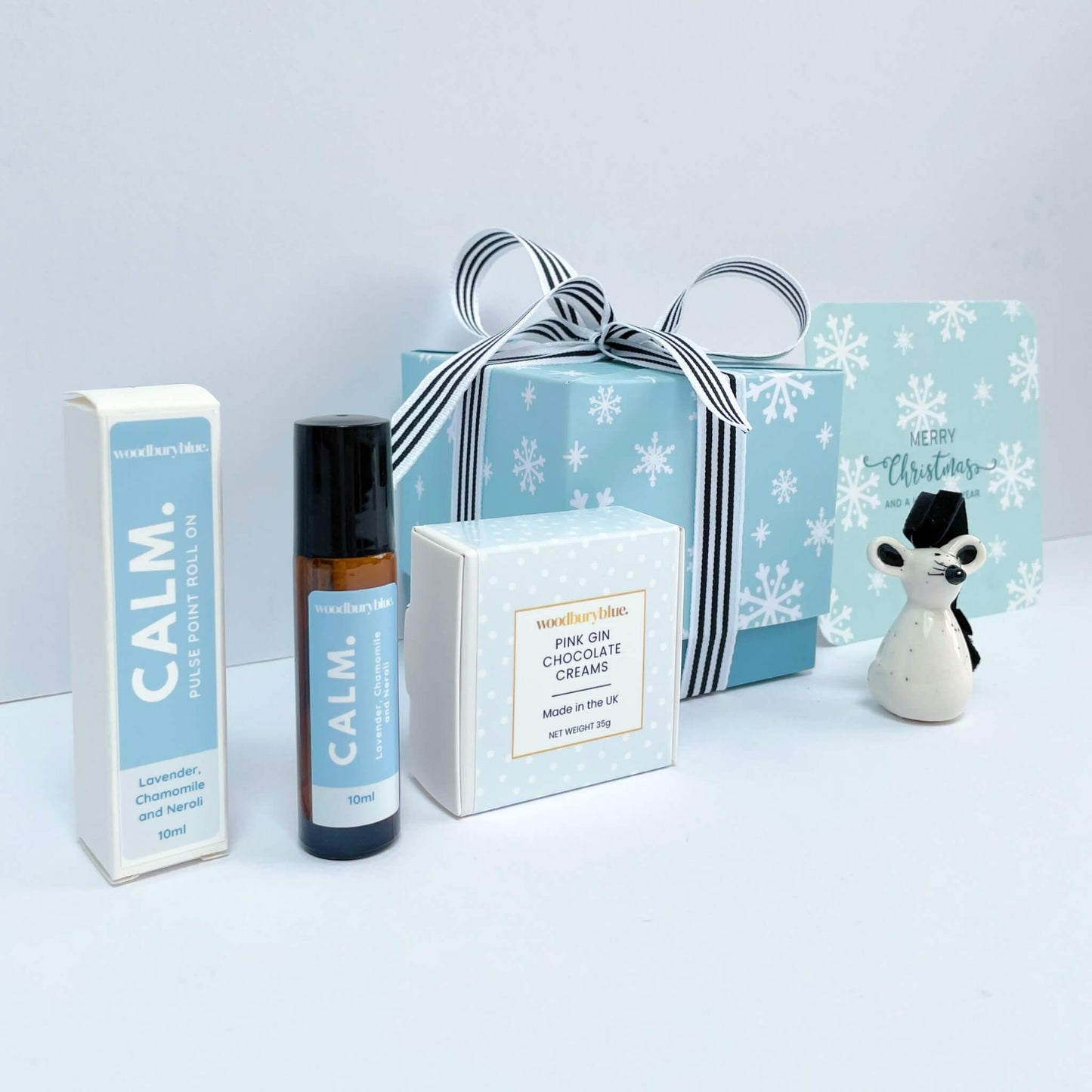 Close-up of Silent Night gift box showing striped ribbon, Calm pulse point roll-on, pink gin chocolates, and mouse decoration.