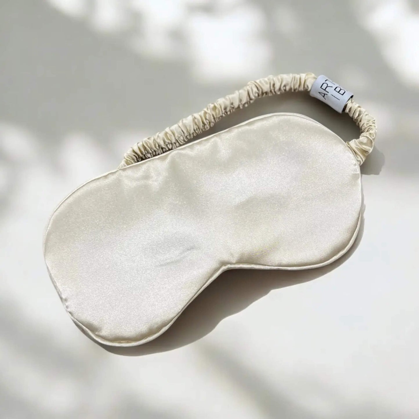 Arthur Betsy sleep mask with ruched satin elastic strap shown on a pale backdrop