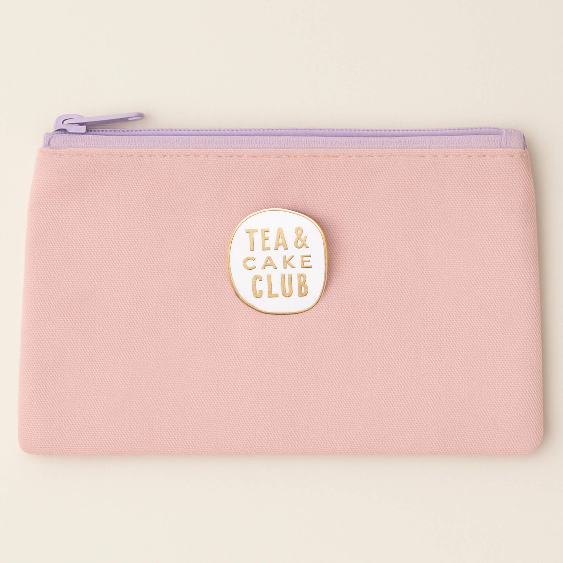 Tea and Cake Club enamel pin badge attached to a pastel pink pencil case with lilac zip.