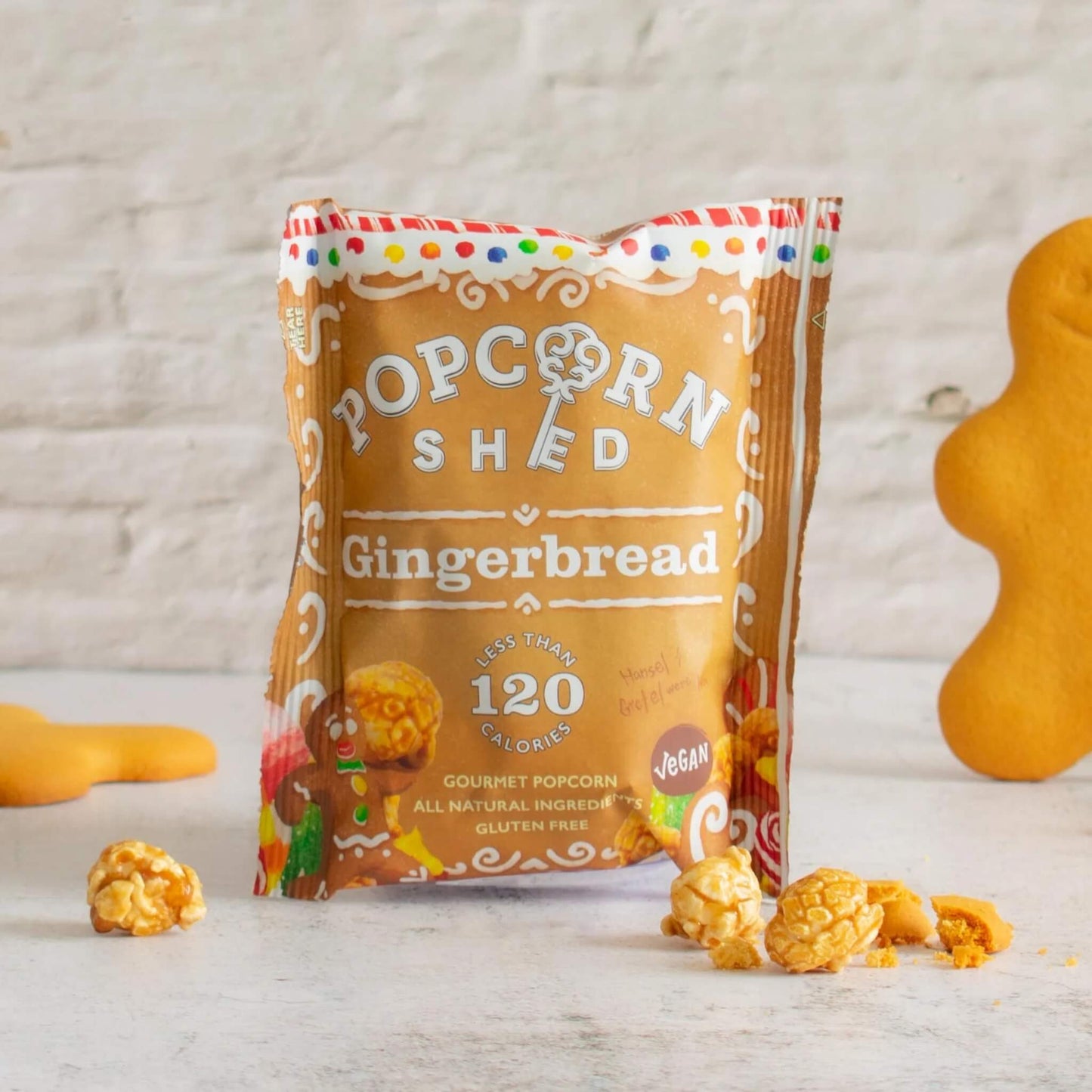 Popcorn Shed Vegan Gingerbread Popcorn snack pack with scattered popcorn and gingerbread biscuits.