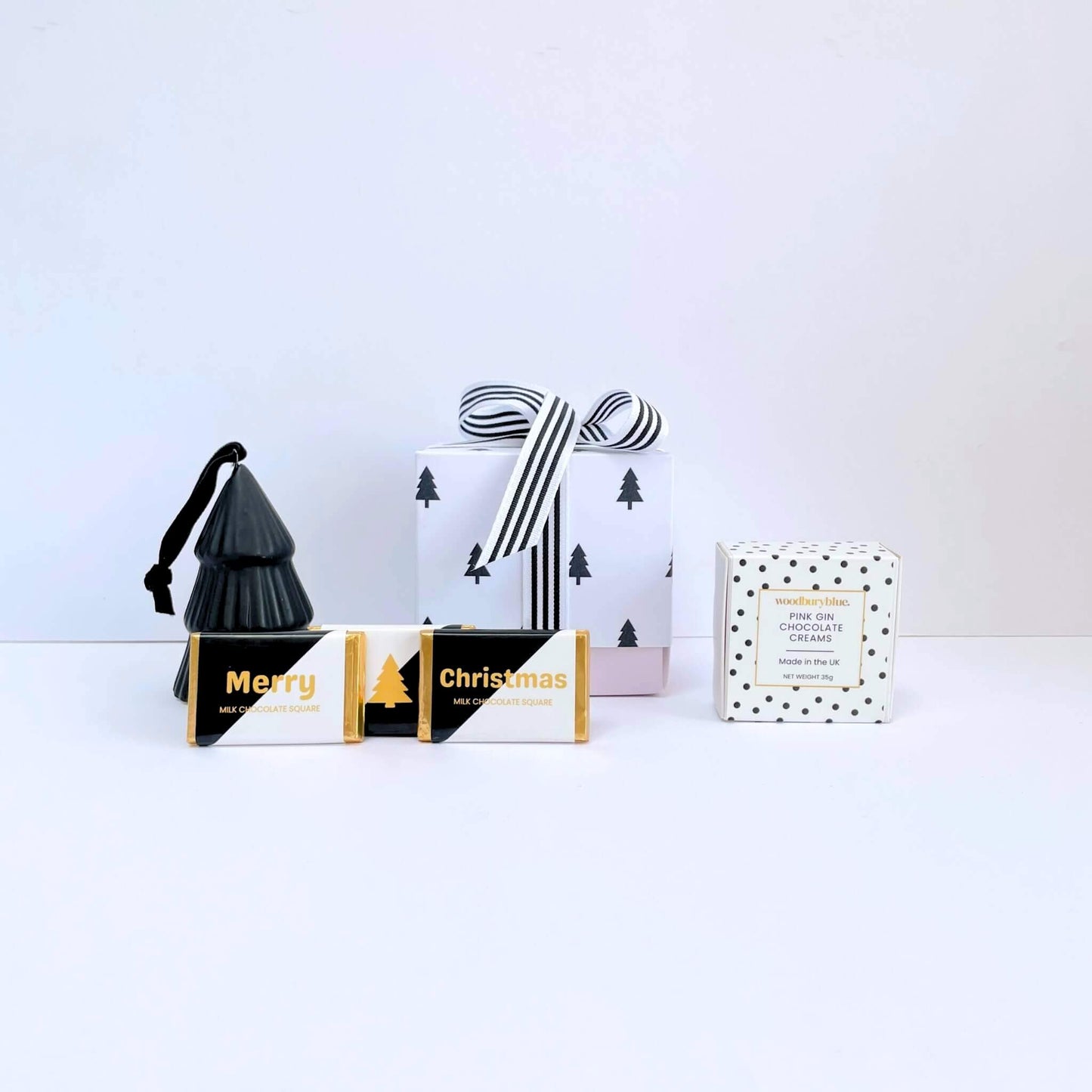 Front view of the White Christmas Gift Box with black ceramic tree ornament, Merry and Christmas chocolate squares, pink gin chocolate creams, and festive gift box tied with monochrome ribbon