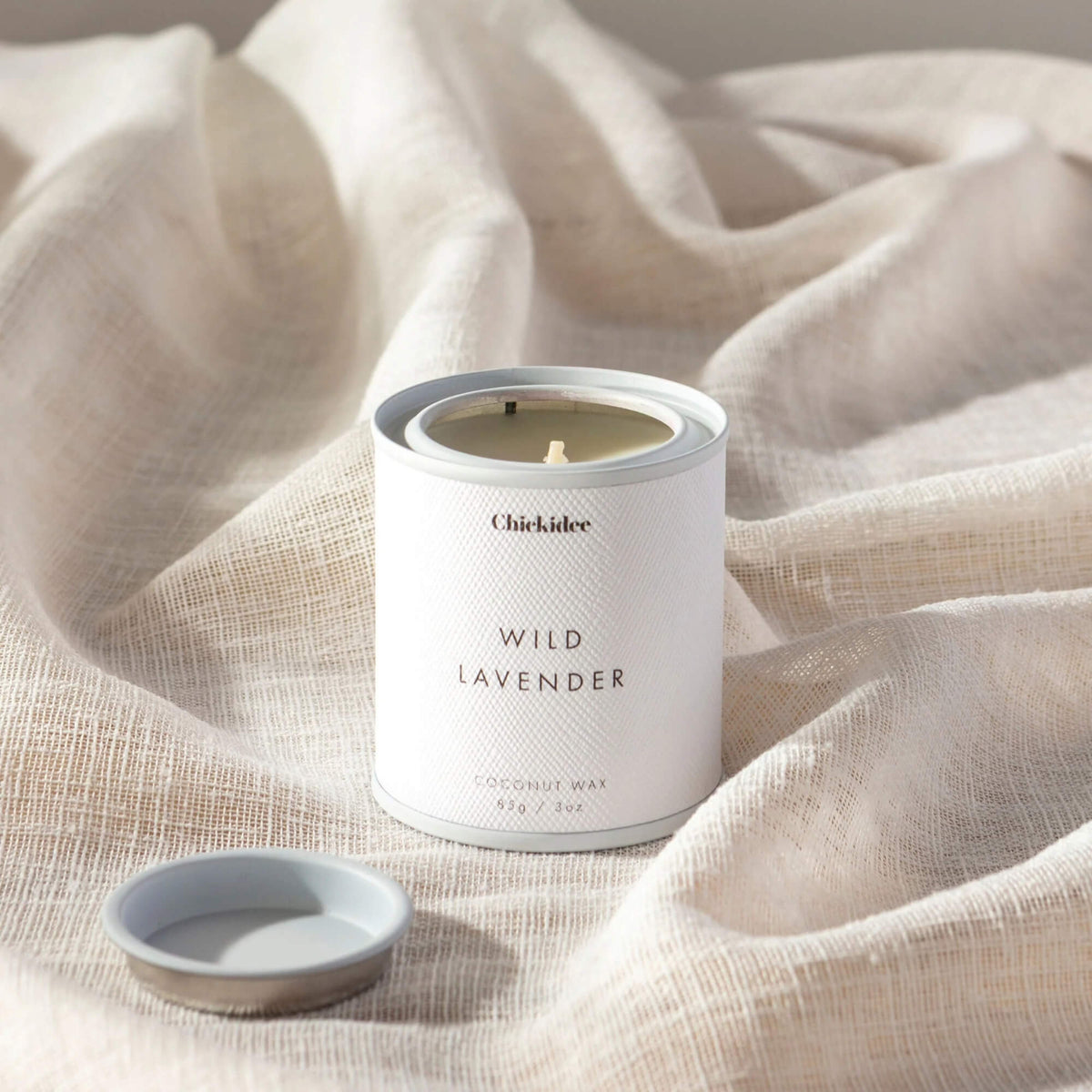 Wild Lavender coconut wax tin candle displayed on pale fabric with its lid beside it