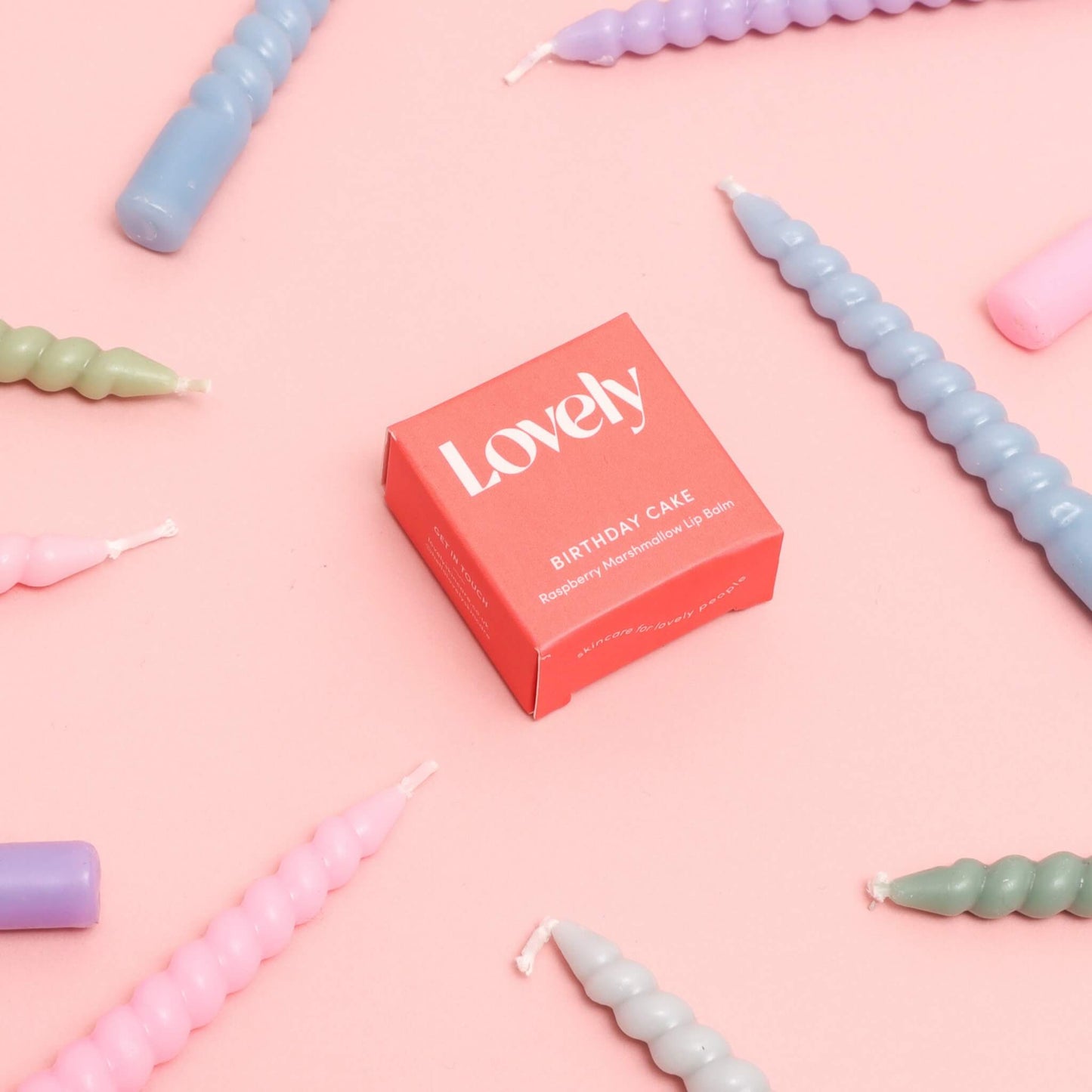 Lovely Skincare Birthday Cake Lip Balm box surrounded by pastel birthday candles on pink background