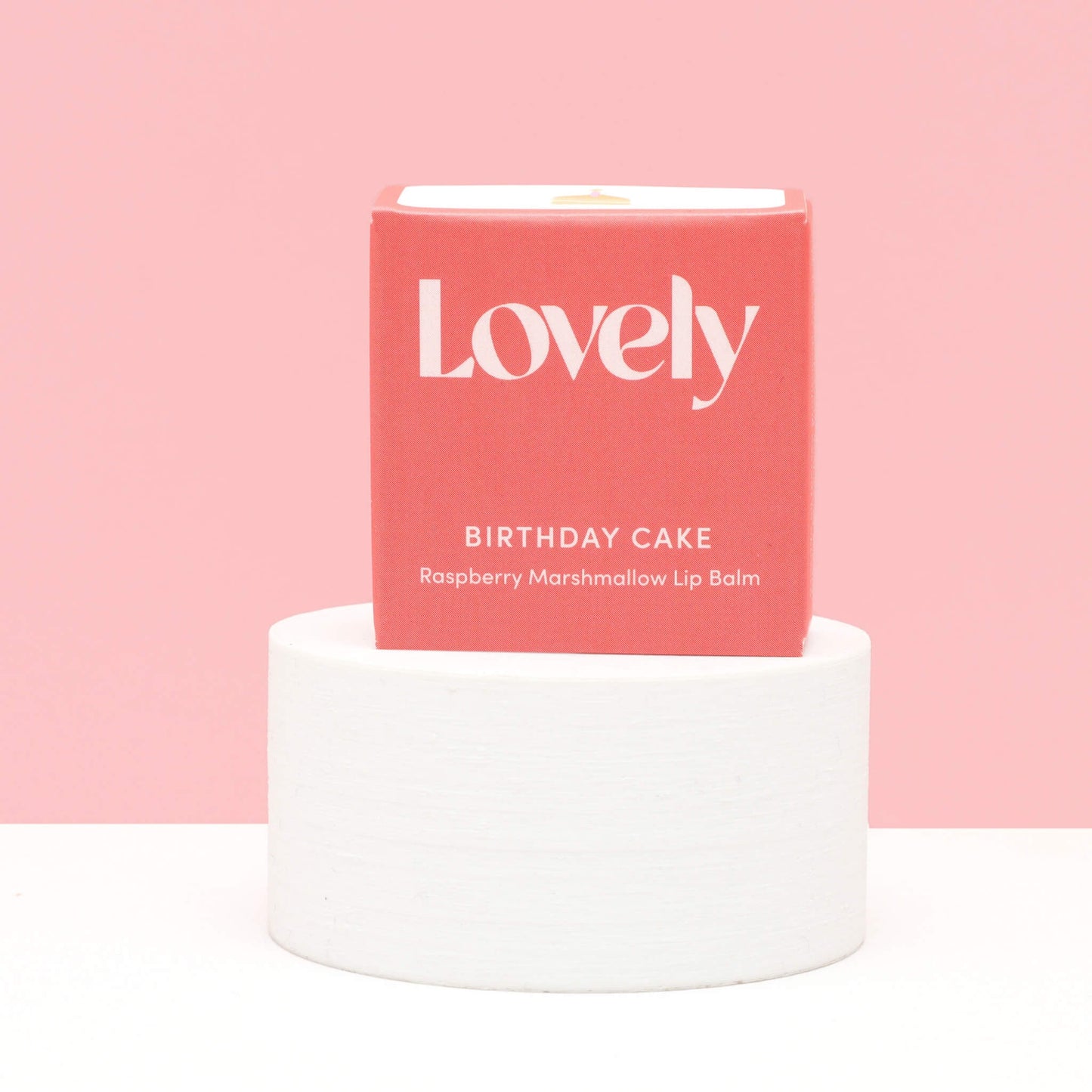 Lovely Skincare Birthday Cake Raspberry Marshmallow Lip Balm box on white plinth against pink background