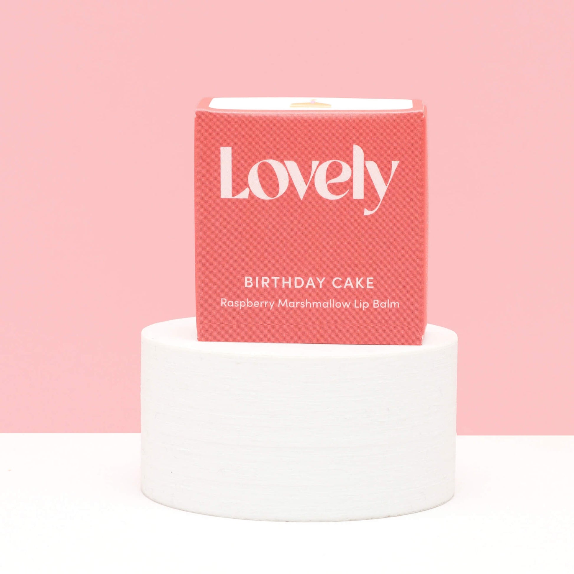 Lovely Skincare Birthday Cake Raspberry Marshmallow Lip Balm box on white plinth against pink background