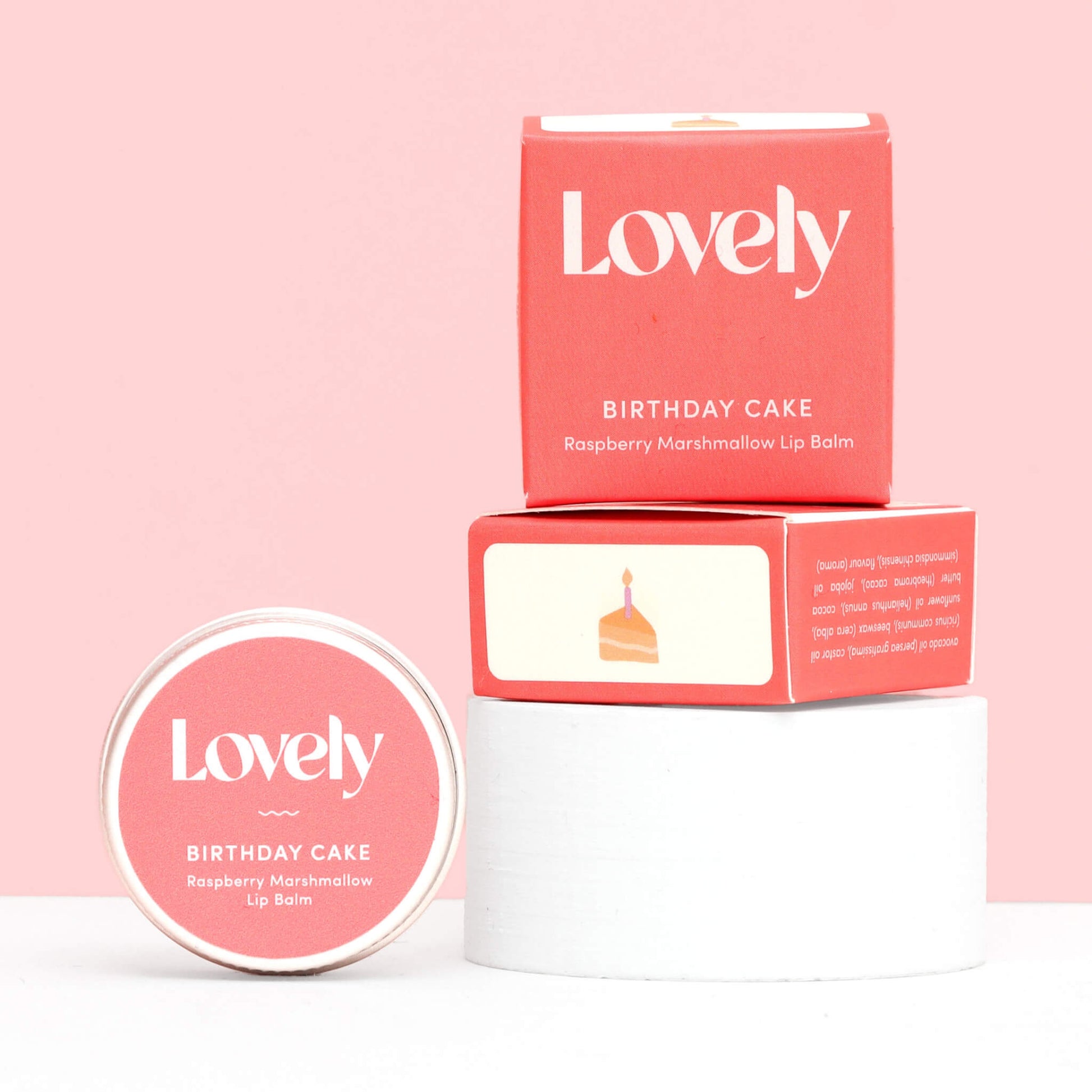 Lovely Skincare Birthday Cake Raspberry Marshmallow Lip Balm tin and box stacked on white stand against pink background