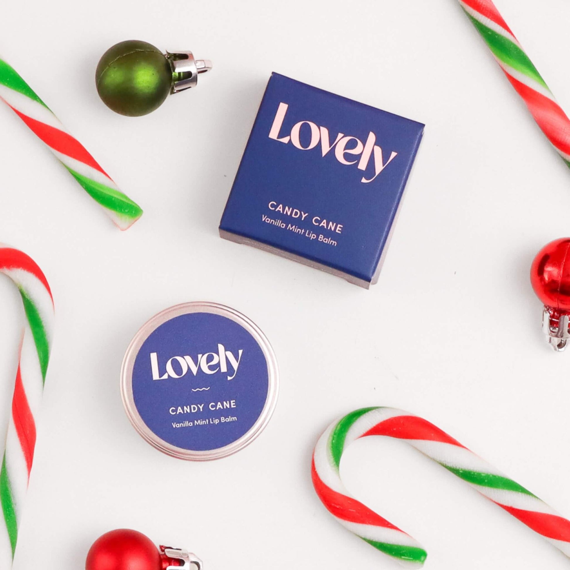 Lovely Skincare Candy Cane Lip Balm with candy canes and red and green baubles on white background