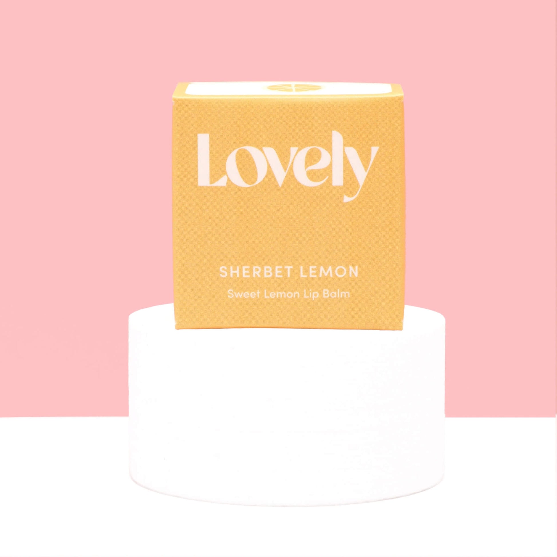 Lovely Skincare Sherbet Lemon Sweet Lemon Lip Balm box on white plinth against soft pink background