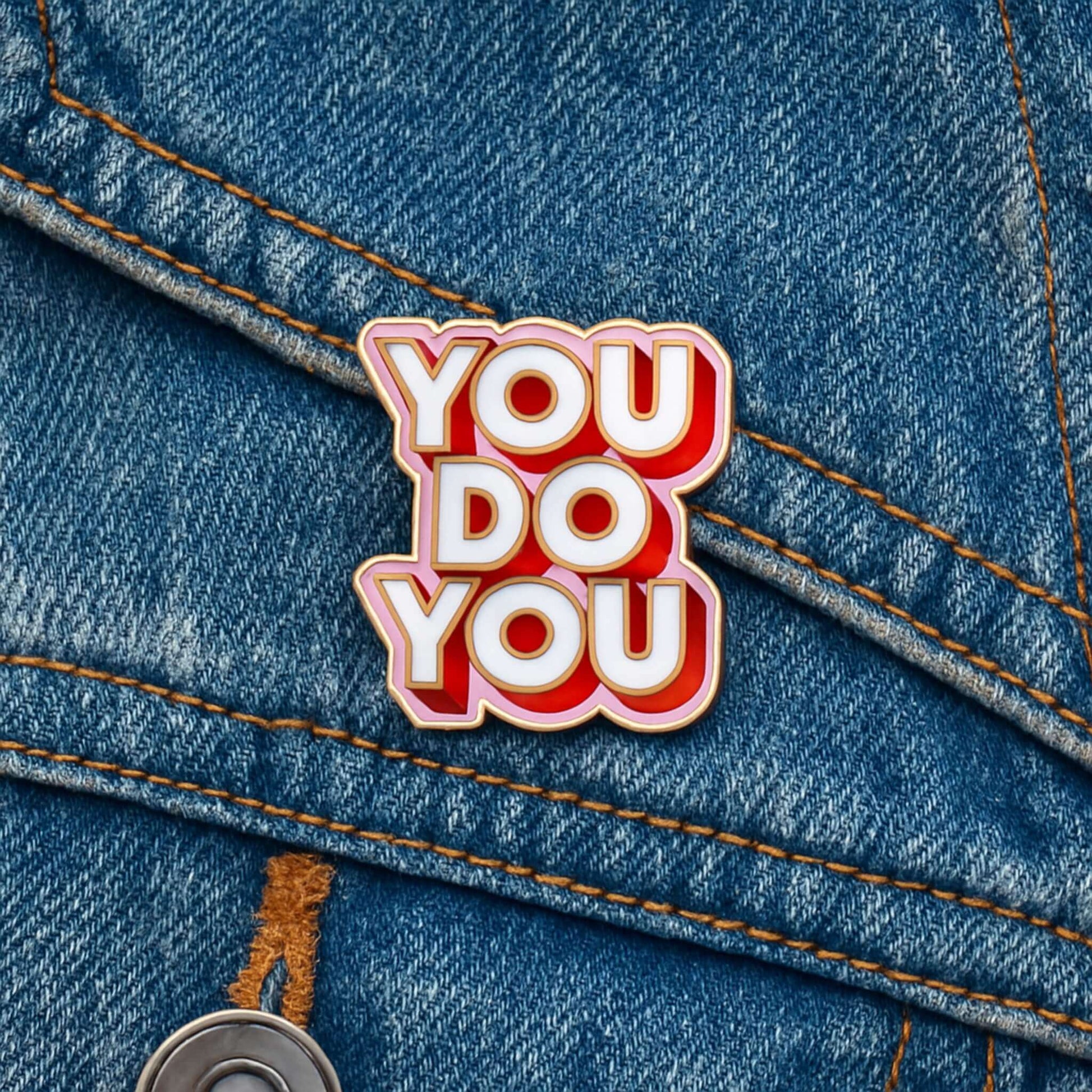 You Do You enamel pin badge with gold edge attached to the pocket of a blue denim jacket with orange stitching