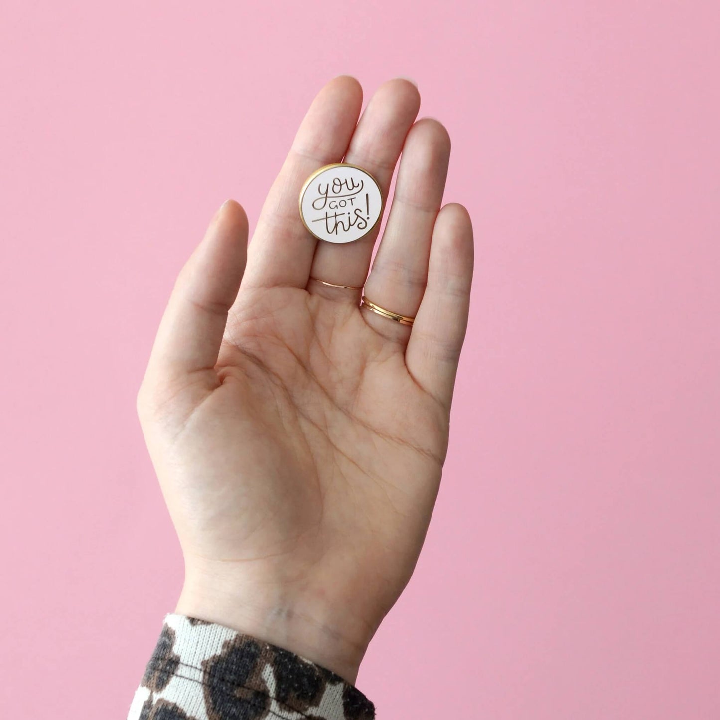 You Got This enamel pin badge resting in an open hand against a pastel pink background.