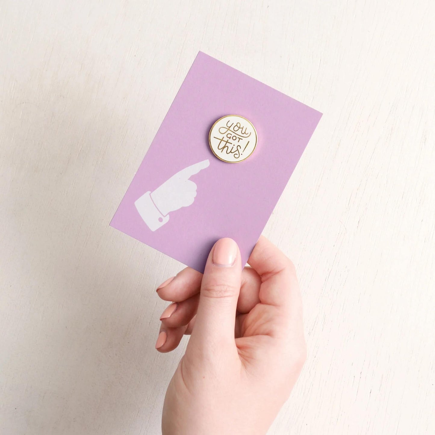 Hand holding purple recycled backing card with You Got This enamel pin badge.