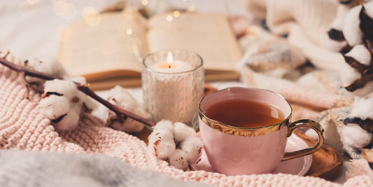 Cosy flat lay of a pink teacup, lit candle and open book on a soft blanket – perfect for a relaxing self-care Sunday at home