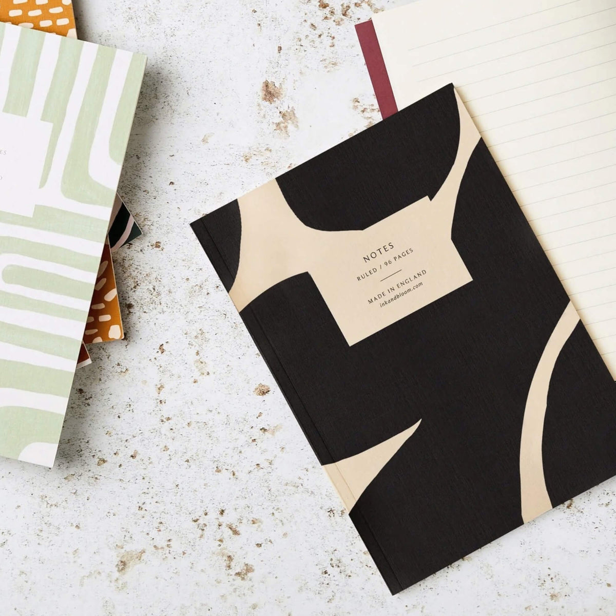 Black and cream A5 notebook beside open off-white ruled pages and other stationery