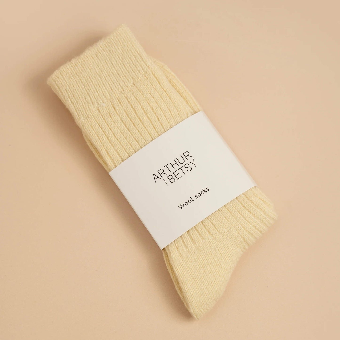 Pack of cream wool socks with a white label on a beige background