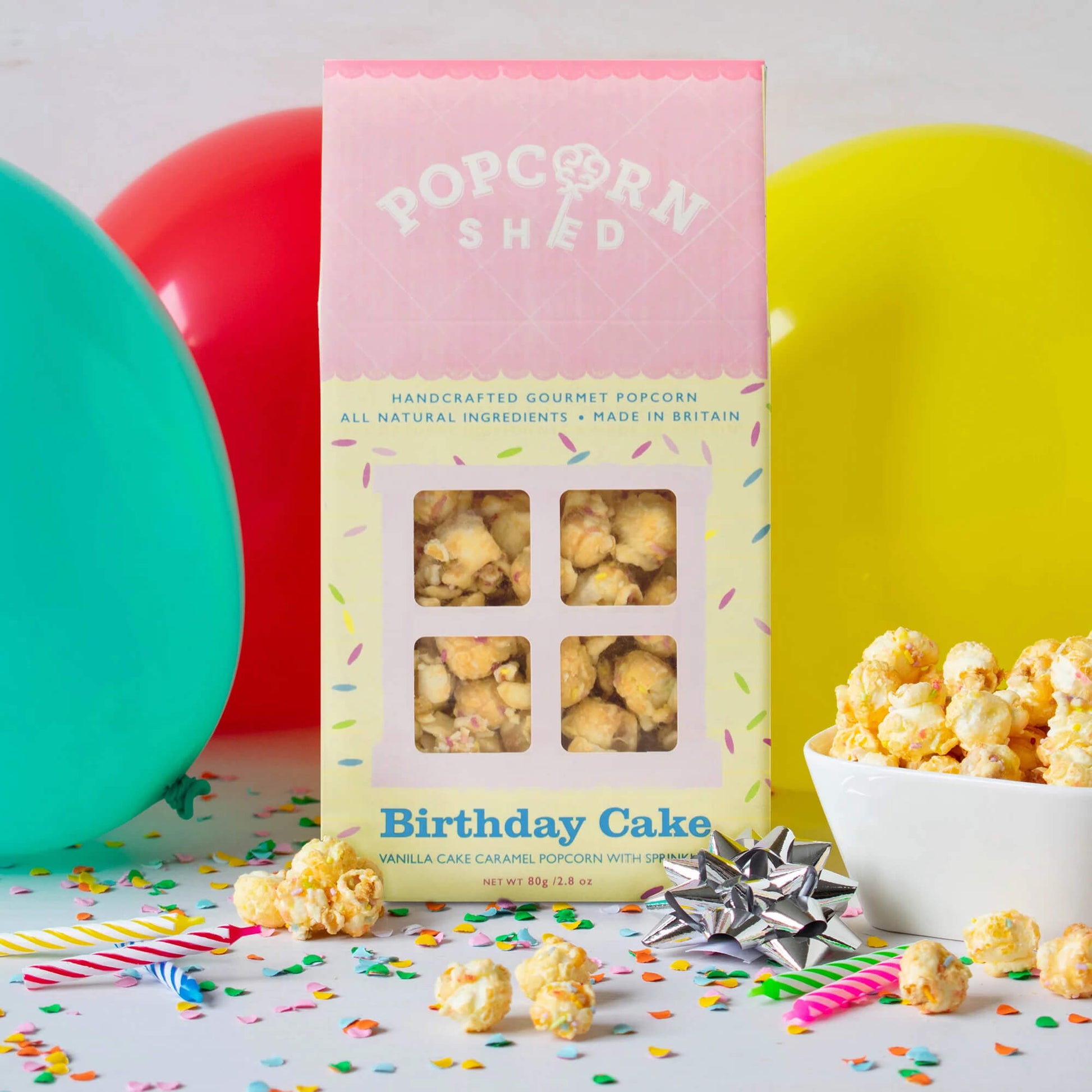 Birthday Cake Gourmet Popcorn gift box displayed with balloons, confetti and a bowl of popcorn for a birthday celebration.