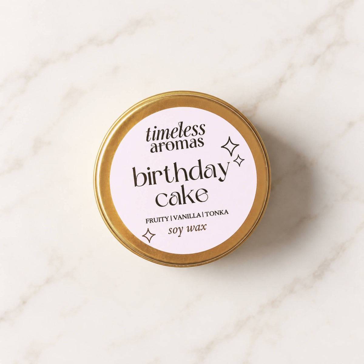 Birthday Cake soy wax candle by Timeless Aromas in a mini gold tin on a light marble background
