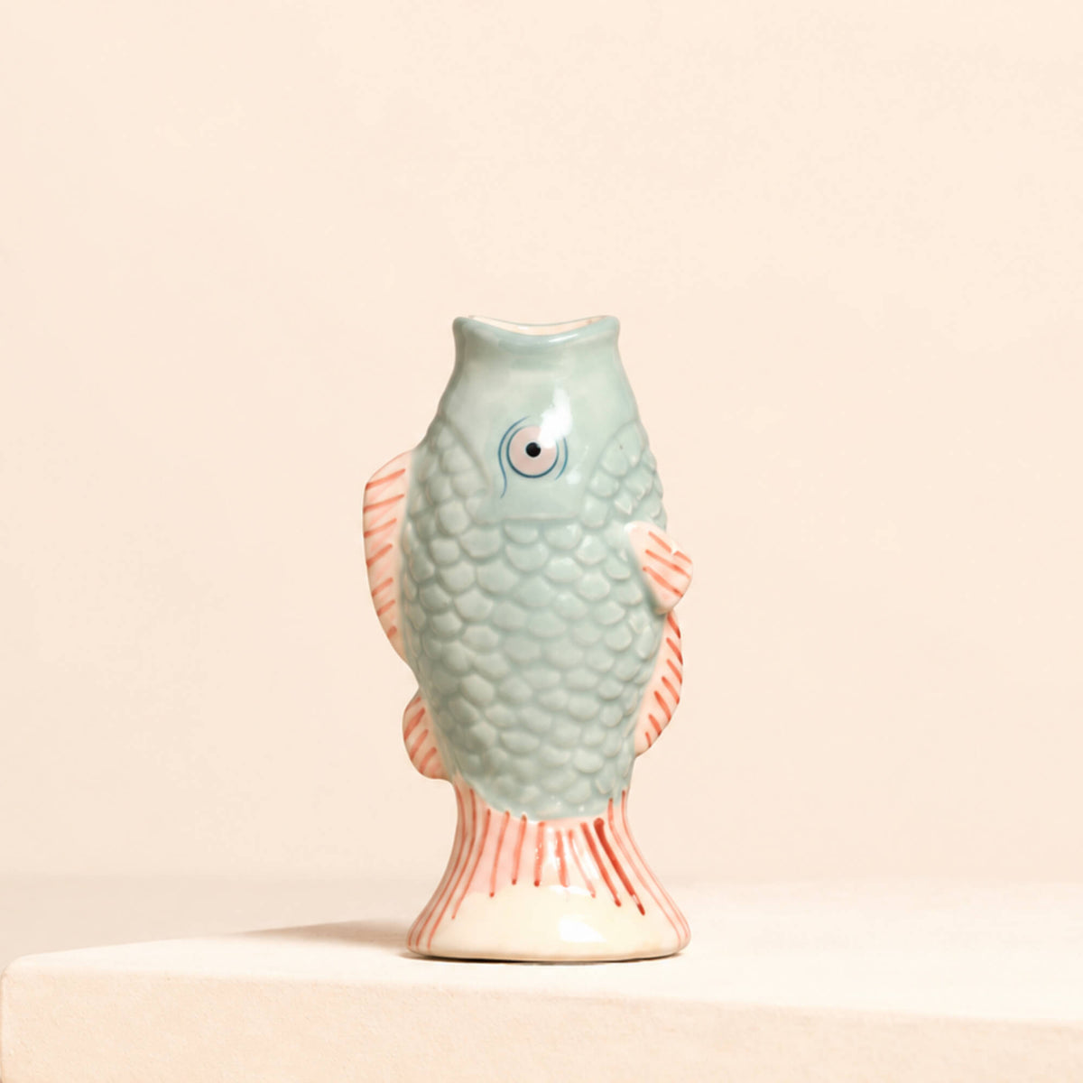 Lisa Angel blue ceramic mini fish bud vase with textured scales and pink striped fins, displayed without flowers against a soft beige background.