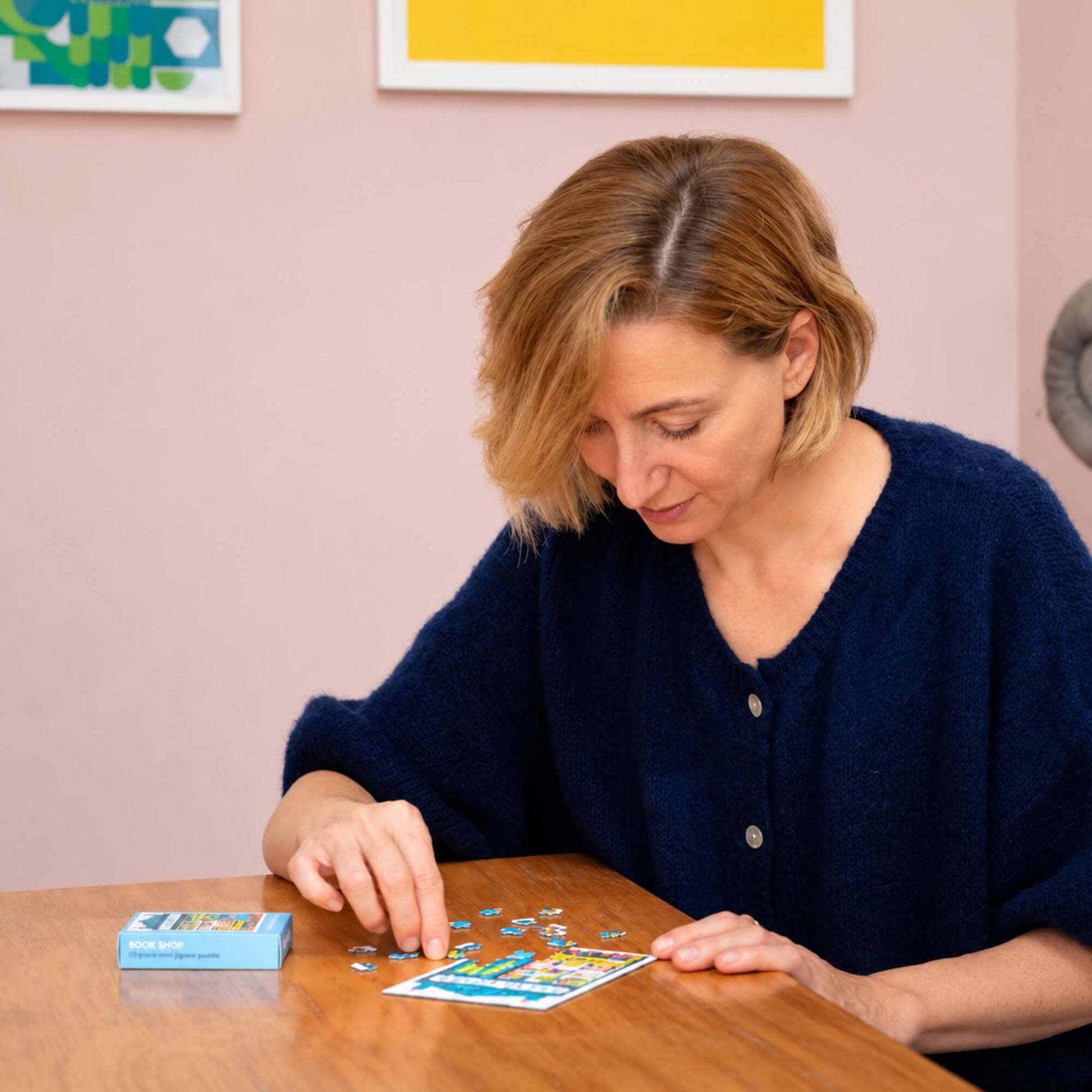 Woman completing the Bookshop mini jigsaw puzzle by Happily Puzzles at a table