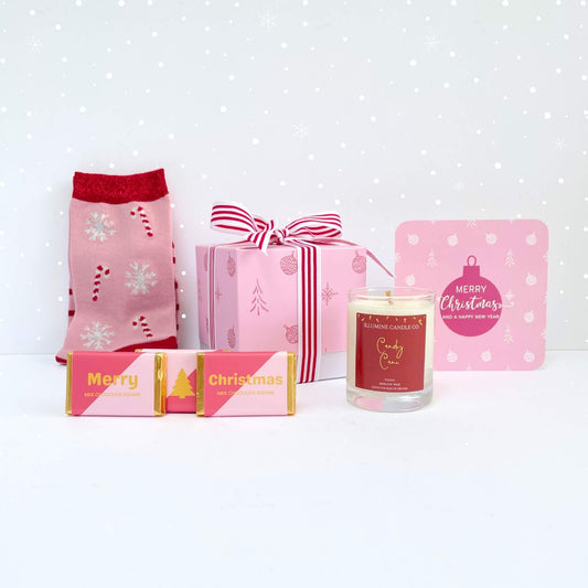 Candy Cane Wishes Gift Box styled with pink festive socks, candy cane-scented candle, pink and gold Merry Christmas chocolates, striped ribbon box, and pink bauble notecard on a snowy background
