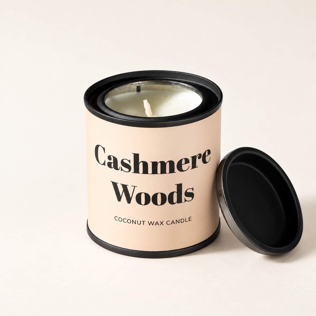 Cashmere Woods coconut wax tin candle with black lid resting beside it
