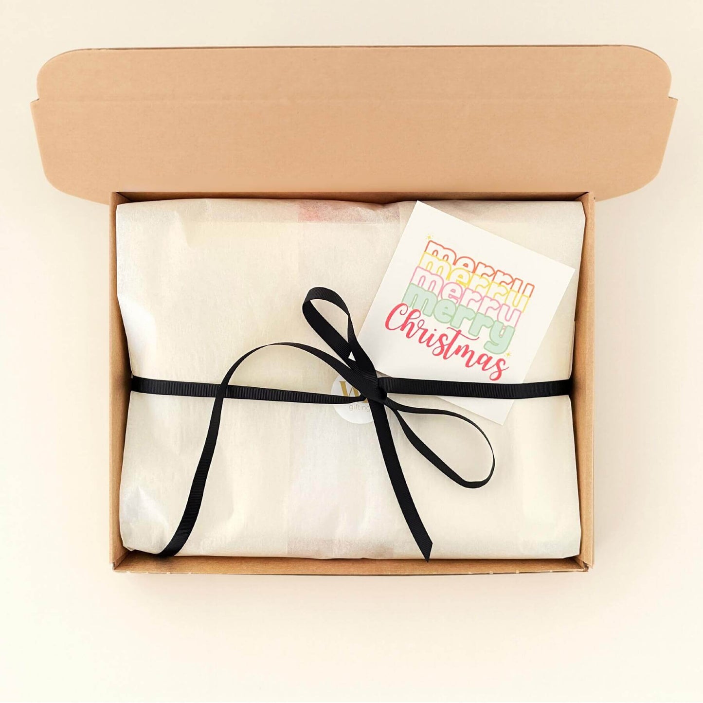 Fireside Treats gift box wrapped in white tissue with a black ribbon and a colourful Merry Christmas card ready to send.