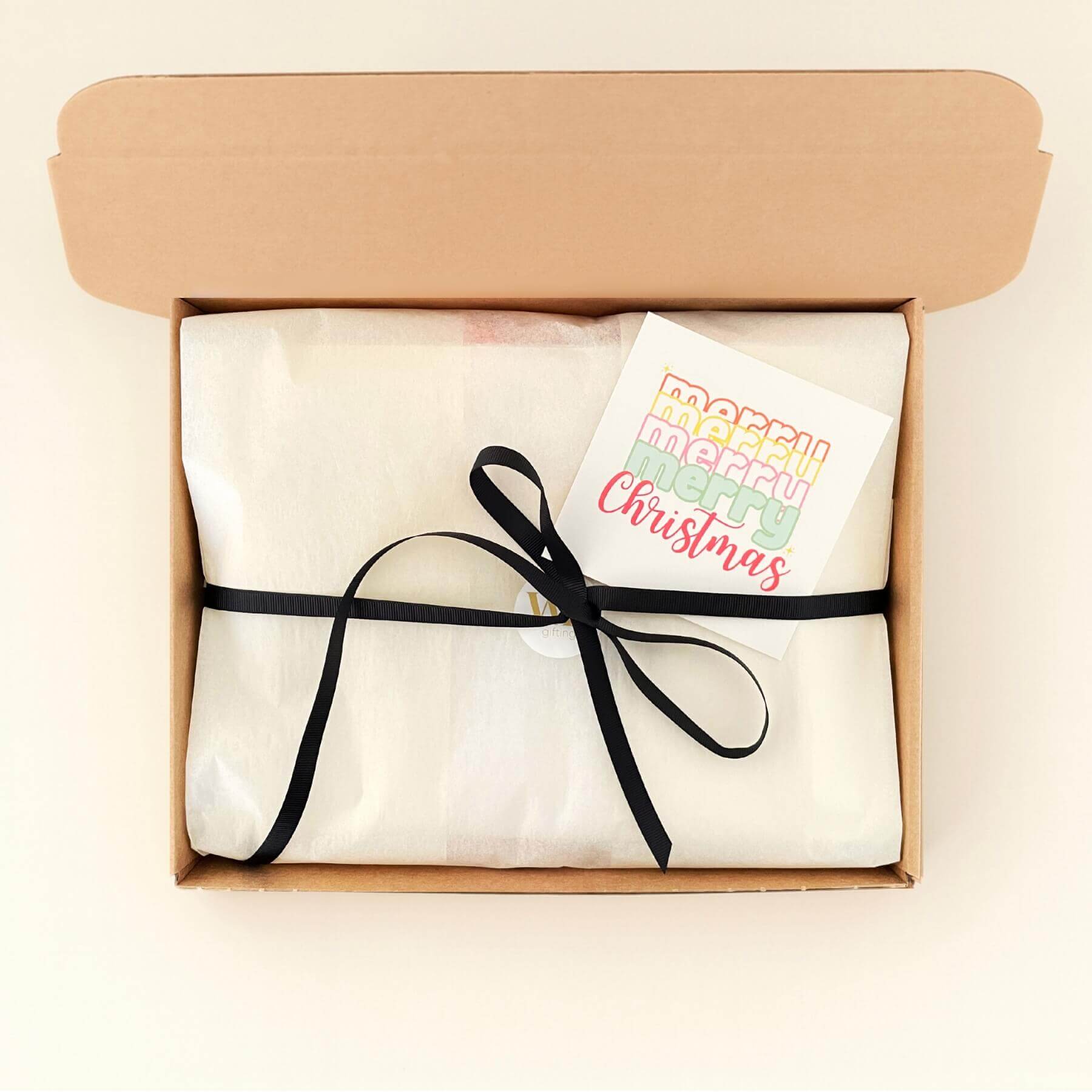 Fireside Treats gift box wrapped in white tissue with a black ribbon and a colourful Merry Christmas card ready to send.