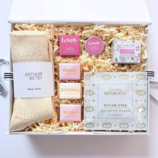 Cosy Birthday Gift Box with cream wool socks, lavender self heating eye mask, blueberry cheesecake lip balm, birthday bath melt and chocolate squares.