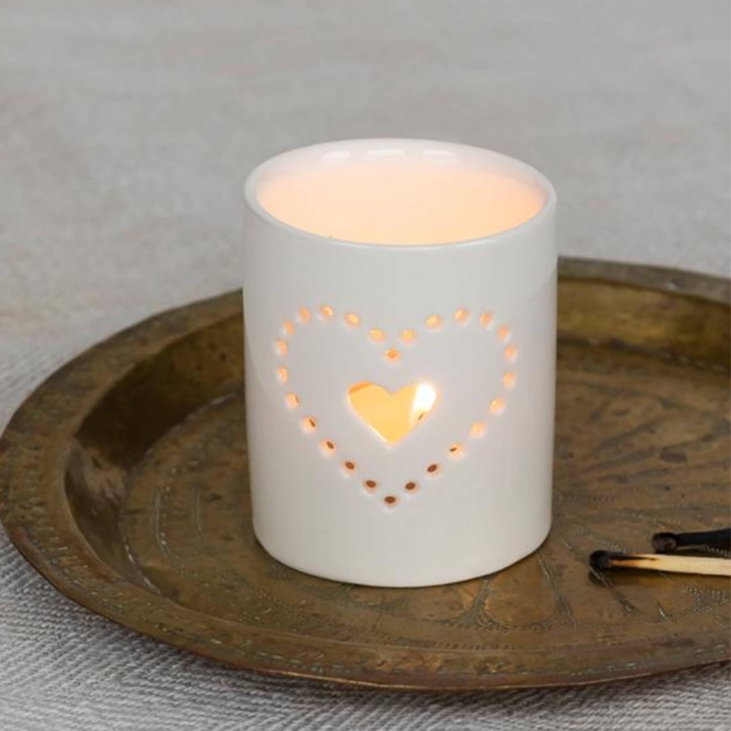 Cream ceramic tealight holder with heart design and a tealight inside, giving a warm and cosy glow