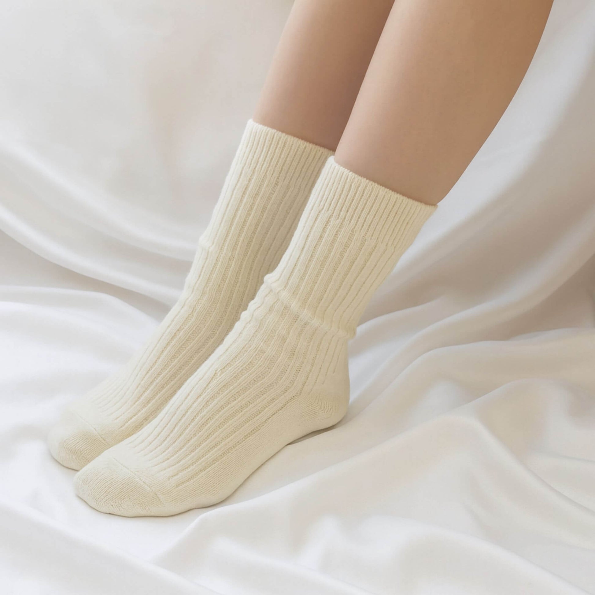 Cream ribbed wool socks being worn, photographed on flowing white fabric for a cosy and modern lifestyle look