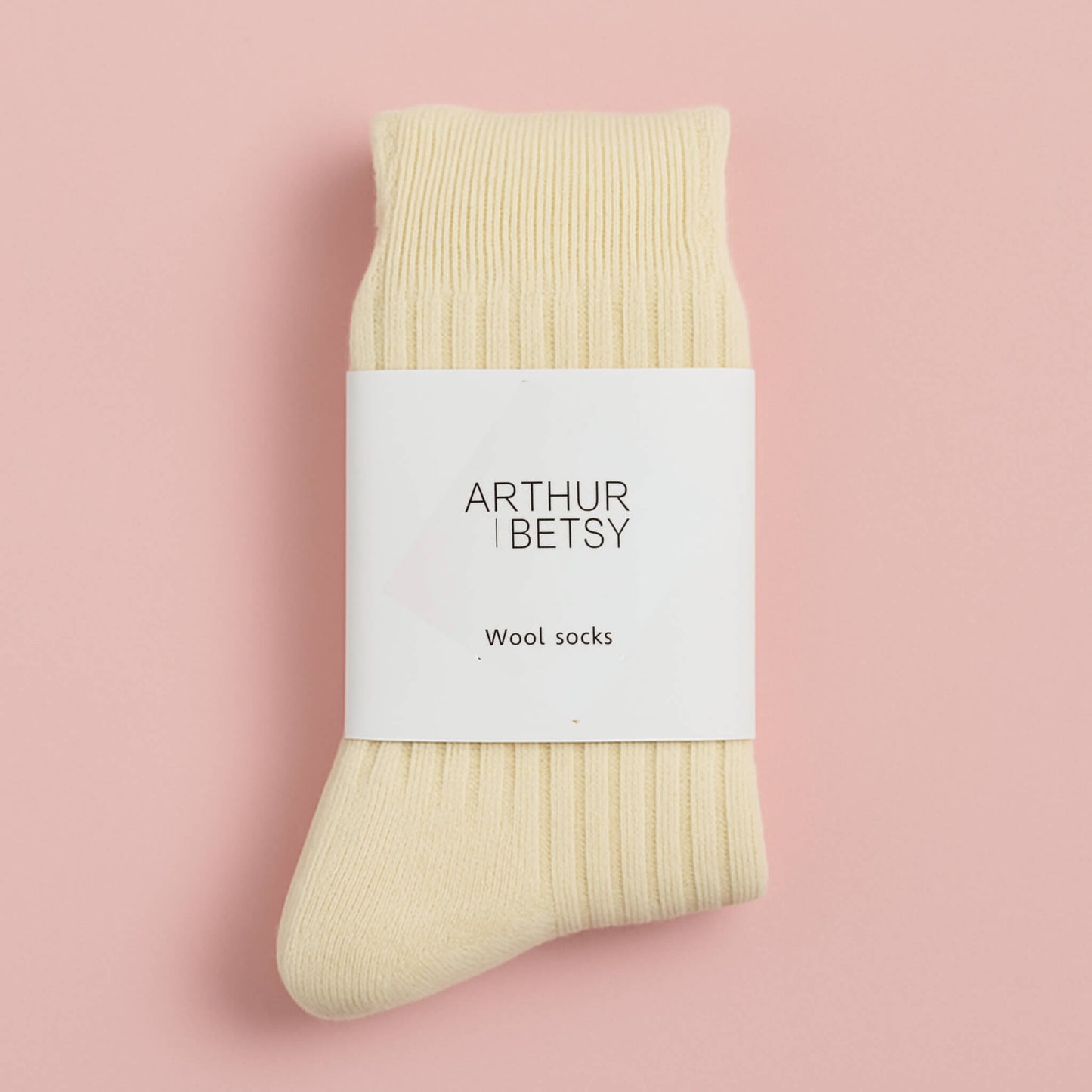 Cream wool socks folded with white branded band, displayed on a soft pastel pink background