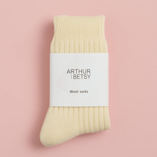 Cream wool socks folded with white branded band, displayed on a soft pastel pink background