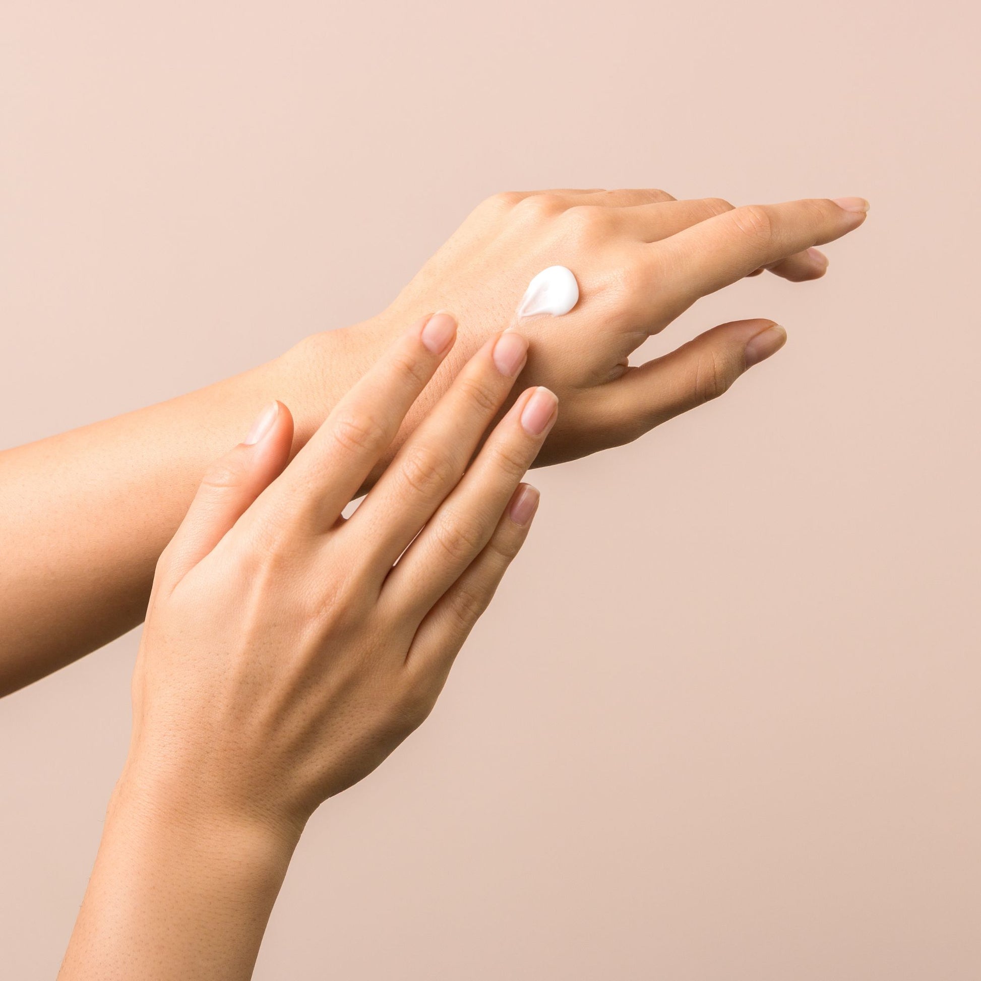 Hand cream being applied to hands on a soft neutral background