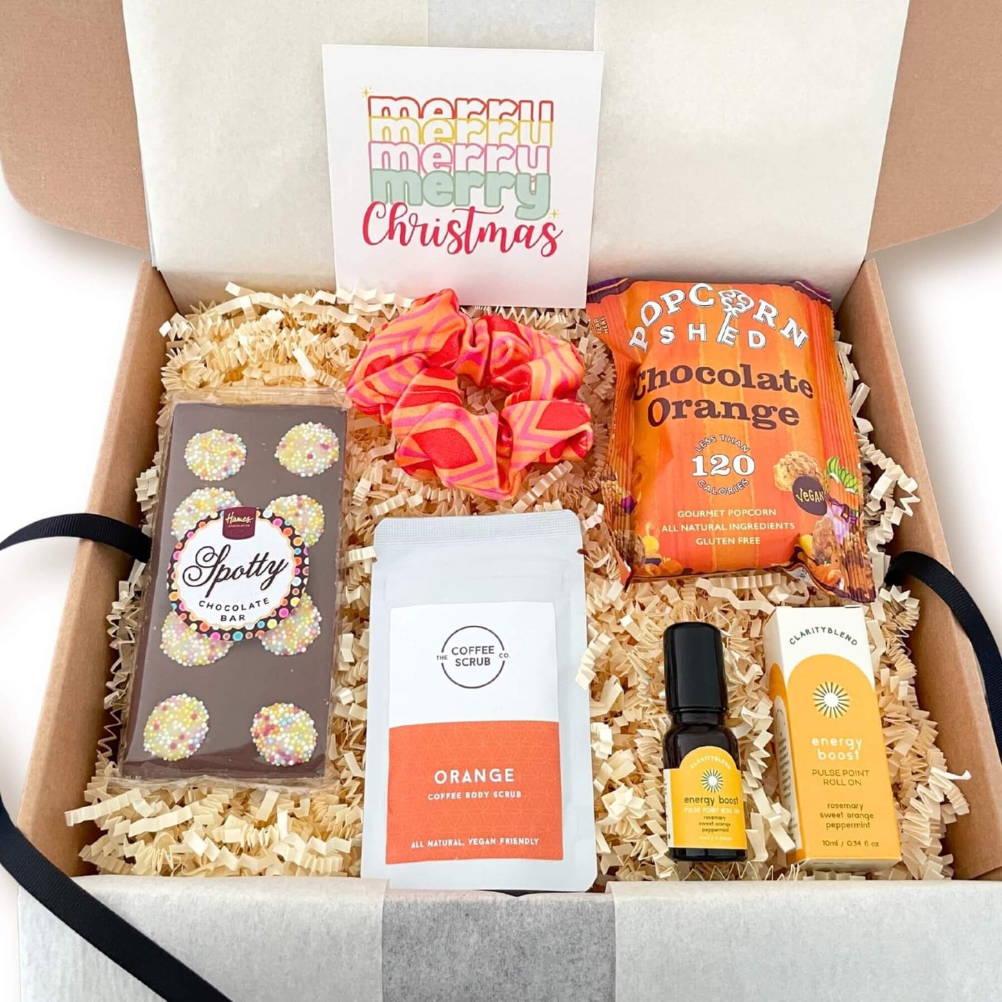 Open Festive Cheer Gift Box showing popcorn, chocolate, scrub, pulse point roll on, scrunchie and Christmas notecard.