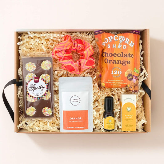 Top down view of the Festive Cheer Gift Box with chocolate orange popcorn, chocolate bar, body scrub, energy roll on and patterned scrunchie.