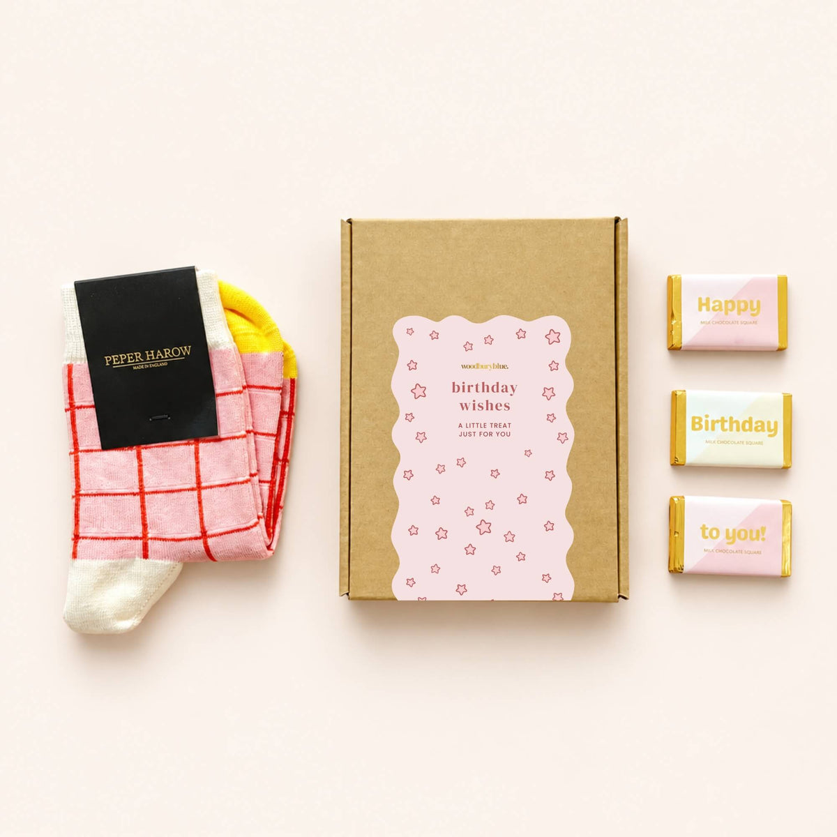 Pink and red checked Peper Harow socks beside a kraft birthday gift box and three milk chocolates with Happy Birthday To You wrappers.