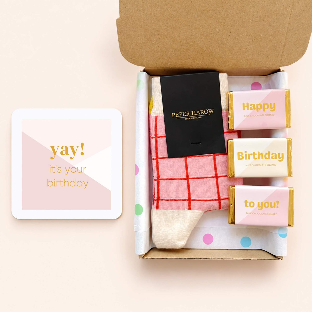 Open birthday gift box containing pink and red checked Peper Harow socks and three milk chocolates, displayed beside a pink Yay It's Your Birthday card.