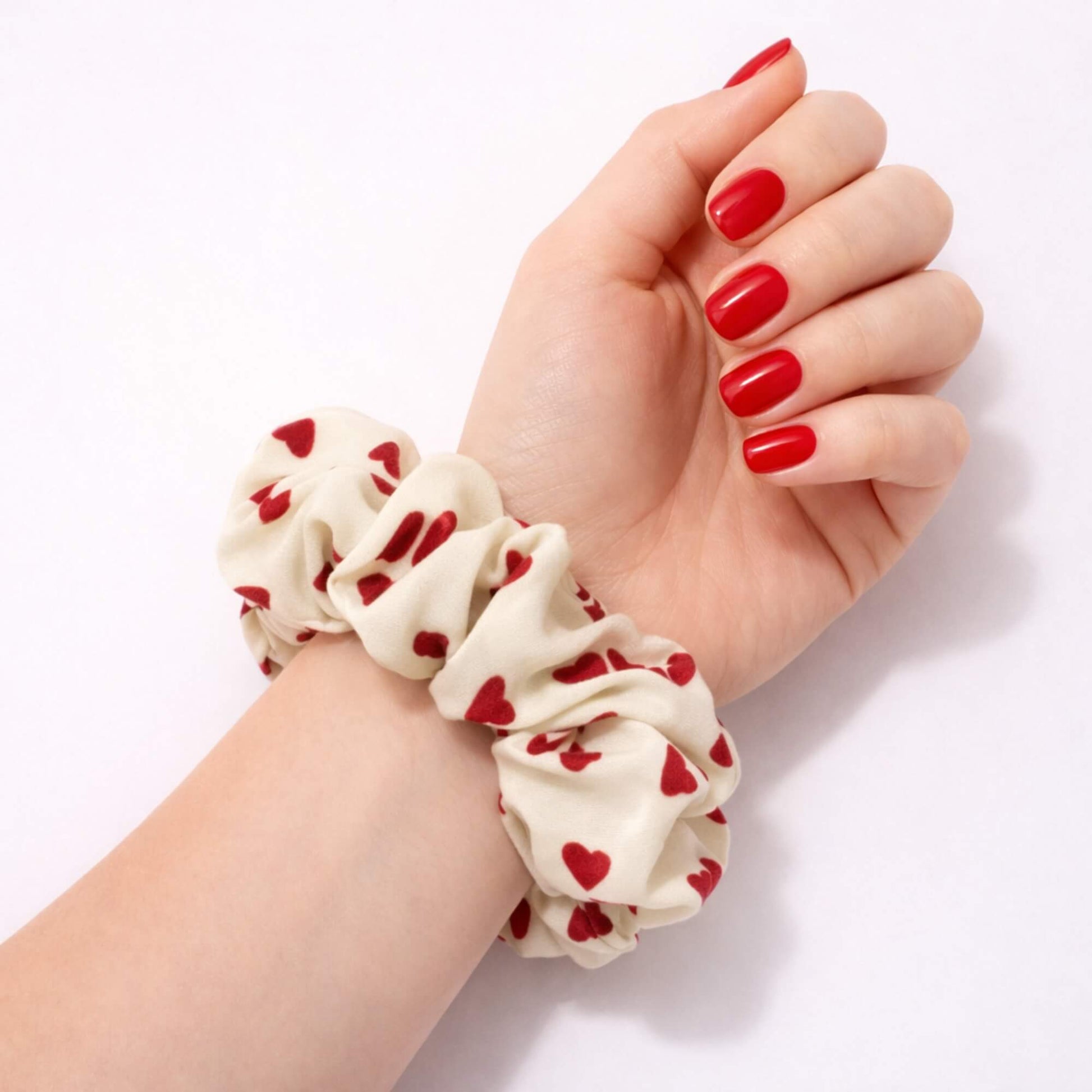 Heart patterned scrunchie worn on a wrist with red nails on a white background