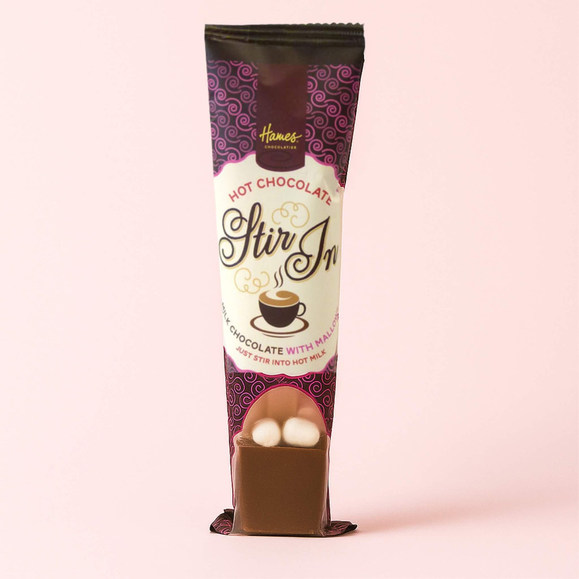 Hot Chocolate Mini Mallow Stirrer standing upright on a pale blush pink background, showing milk chocolate block with two mini marshmallows.